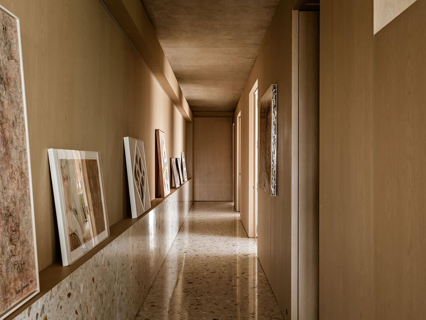 A modern corridor with minimalist design, featuring framed artwork on a wall and light illuminating the space. A modern corridor with minimalist design, featuring framed artwork on a wall and light illuminating the space.