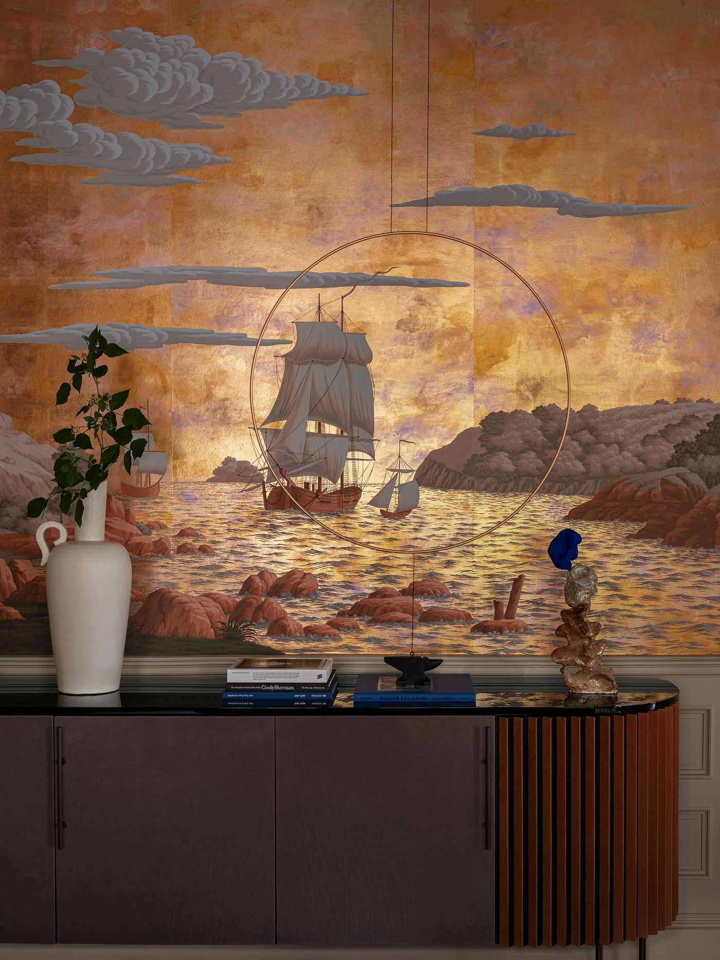 Elegant interior featuring a ship mural against a golden backdrop, with decorative vases and art objects on a sleek sideboard. Elegant interior featuring a ship mural against a golden backdrop, with decorative vases and art objects on a sleek sideboard.