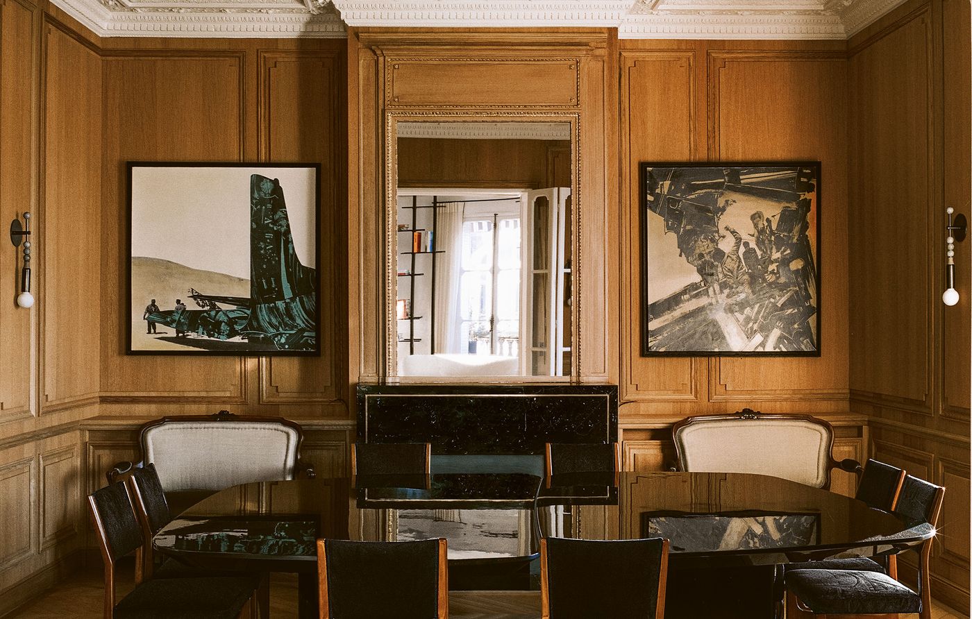 An elegant dining room features rich, warm wooden paneling covering the walls, creating a sense of intimate grandeur. A large, ornate mirror above a dark marble fireplace mantel reflects the room, flanked by two abstract modern artworks, complementing the dark dining table and classic upholstered chairs. An elegant dining room features rich, warm wooden paneling covering the walls, creating a sense of intimate grandeur. A large, ornate mirror above a dark marble fireplace mantel reflects the room, flanked by two abstract modern artworks, complementing the dark dining table and classic upholstered chairs.