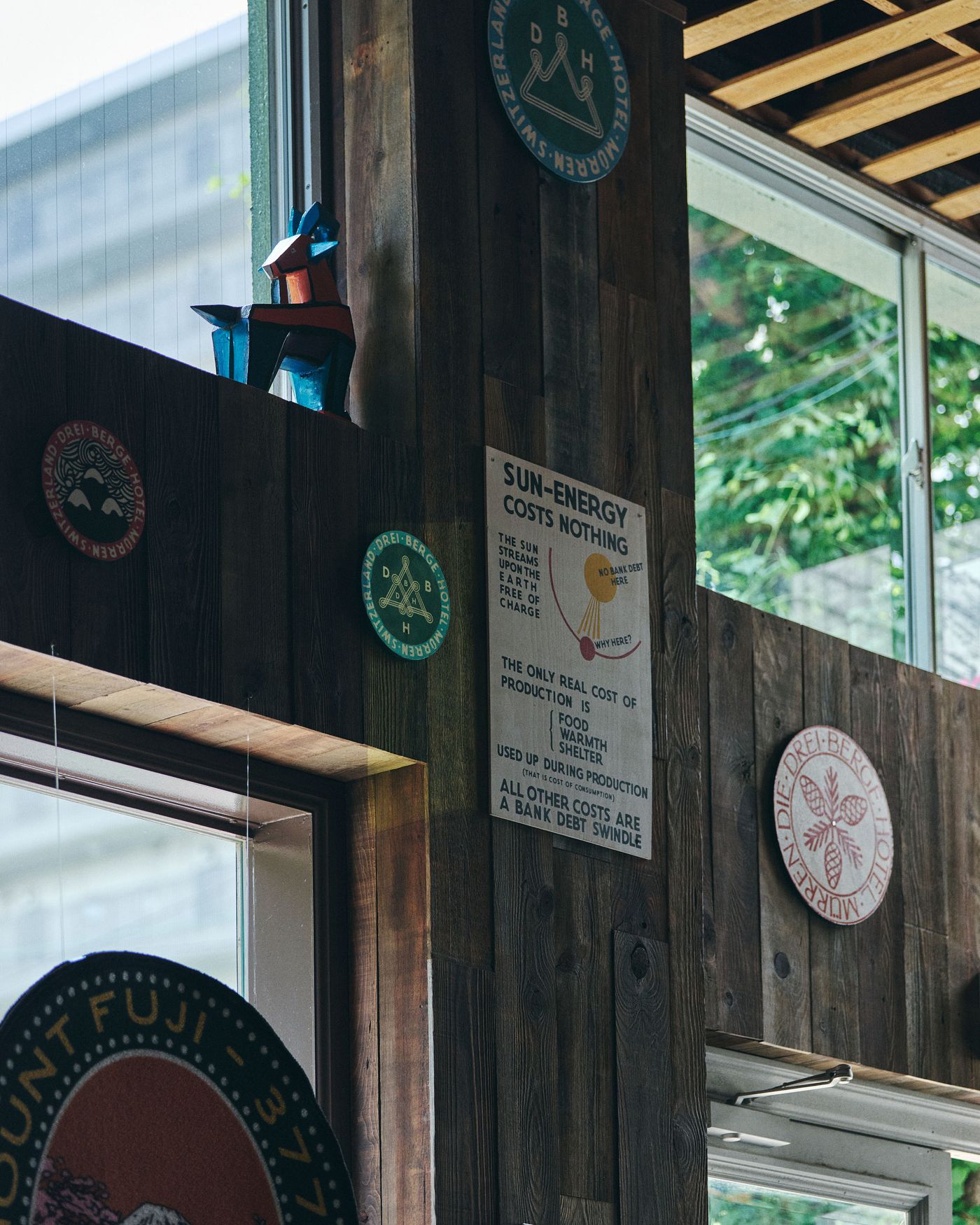 A colorful geometric sculpture sits on a wooden ledge, surrounded by various badges and a sign about the cost of sun energy.