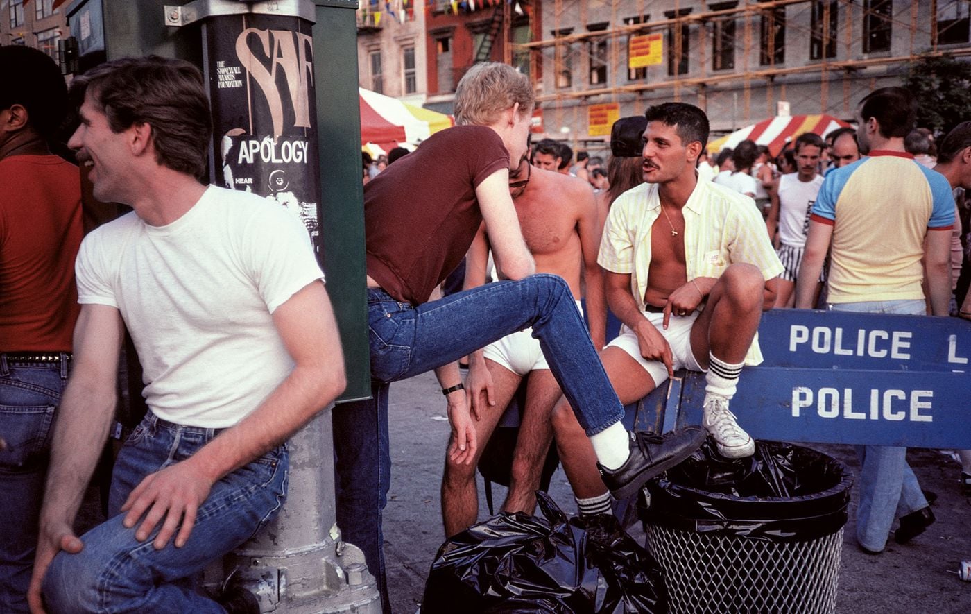 A sun-drenched colour photograph by Stanley Stellar shows men gathering at what appears to be a Pride street fair. One perches on a blue police barricade in white briefs and an open striped shirt, another in jeans props his foot on a rubbish bin, while candy-striped tents, scaffolding and bunting frame the easy camaraderie. A sun-drenched colour photograph by Stanley Stellar shows men gathering at what appears to be a Pride street fair. One perches on a blue police barricade in white briefs and an open striped shirt, another in jeans props his foot on a rubbish bin, while candy-striped tents, scaffolding and bunting frame the easy camaraderie.