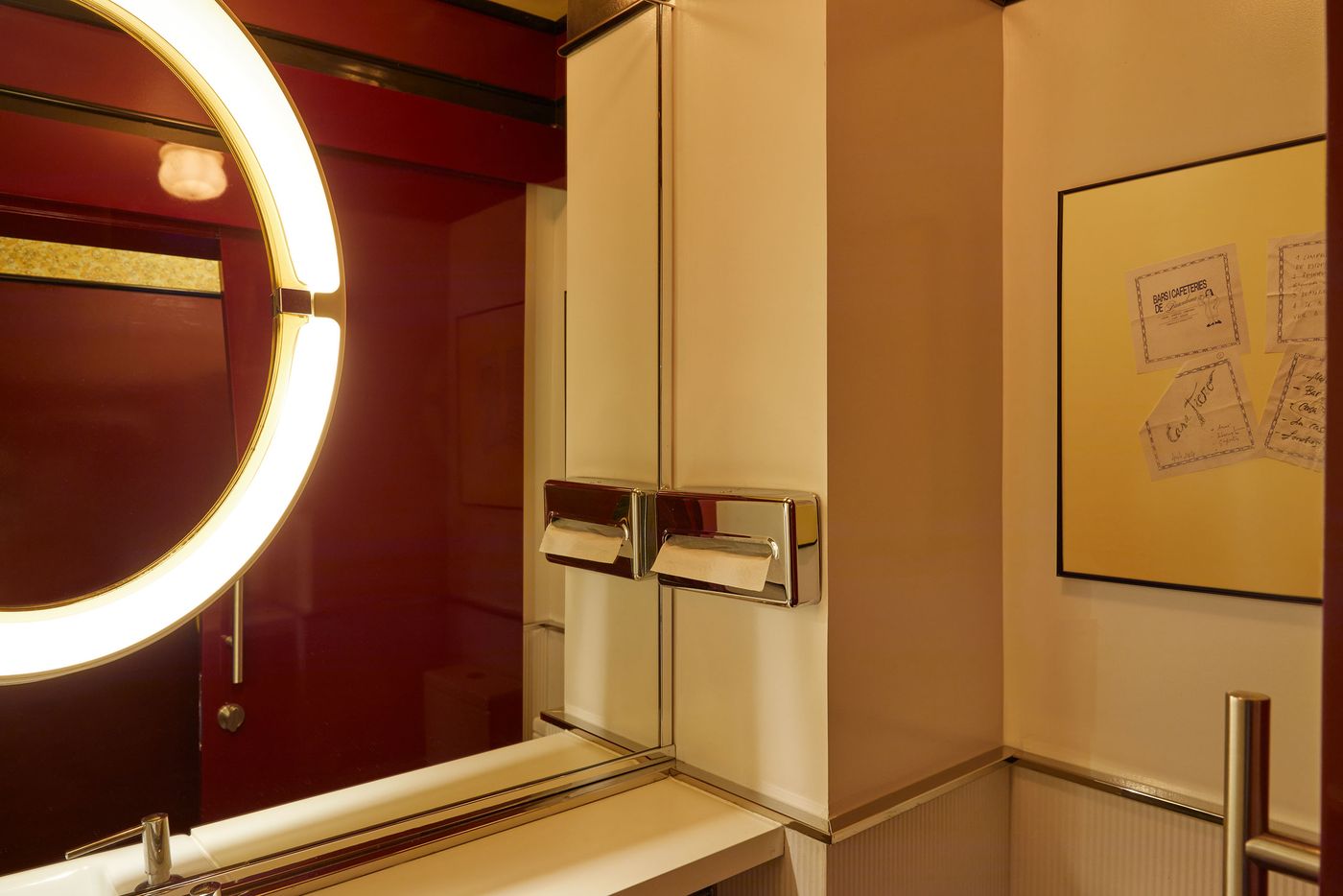 A vibrant and unconventional bathroom interior. The scene is dominated by a circular, glowing light fixture and a large mirror reflecting a deep red wall. A sleek, white cabinet and framed artwork with handwritten notes add layers of detail, creating a playful yet refined atmosphere. A vibrant and unconventional bathroom interior. The scene is dominated by a circular, glowing light fixture and a large mirror reflecting a deep red wall. A sleek, white cabinet and framed artwork with handwritten notes add layers of detail, creating a playful yet refined atmosphere.