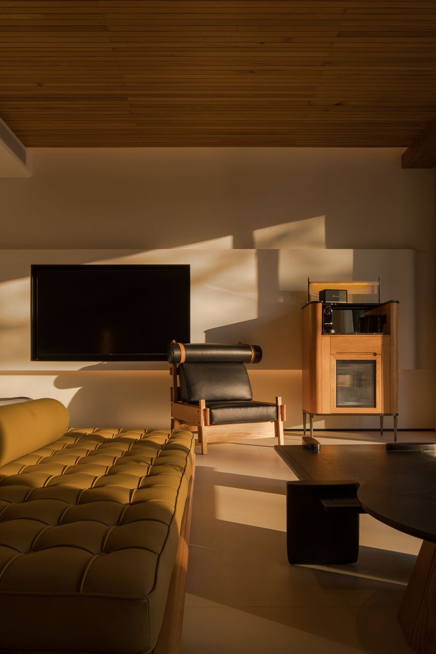 Modern living room with a yellow tufted sofa, a black leather chair, a sleek TV, and a wooden cabinet, illuminated by warm sunlight. Modern living room with a yellow tufted sofa, a black leather chair, a sleek TV, and a wooden cabinet, illuminated by warm sunlight.