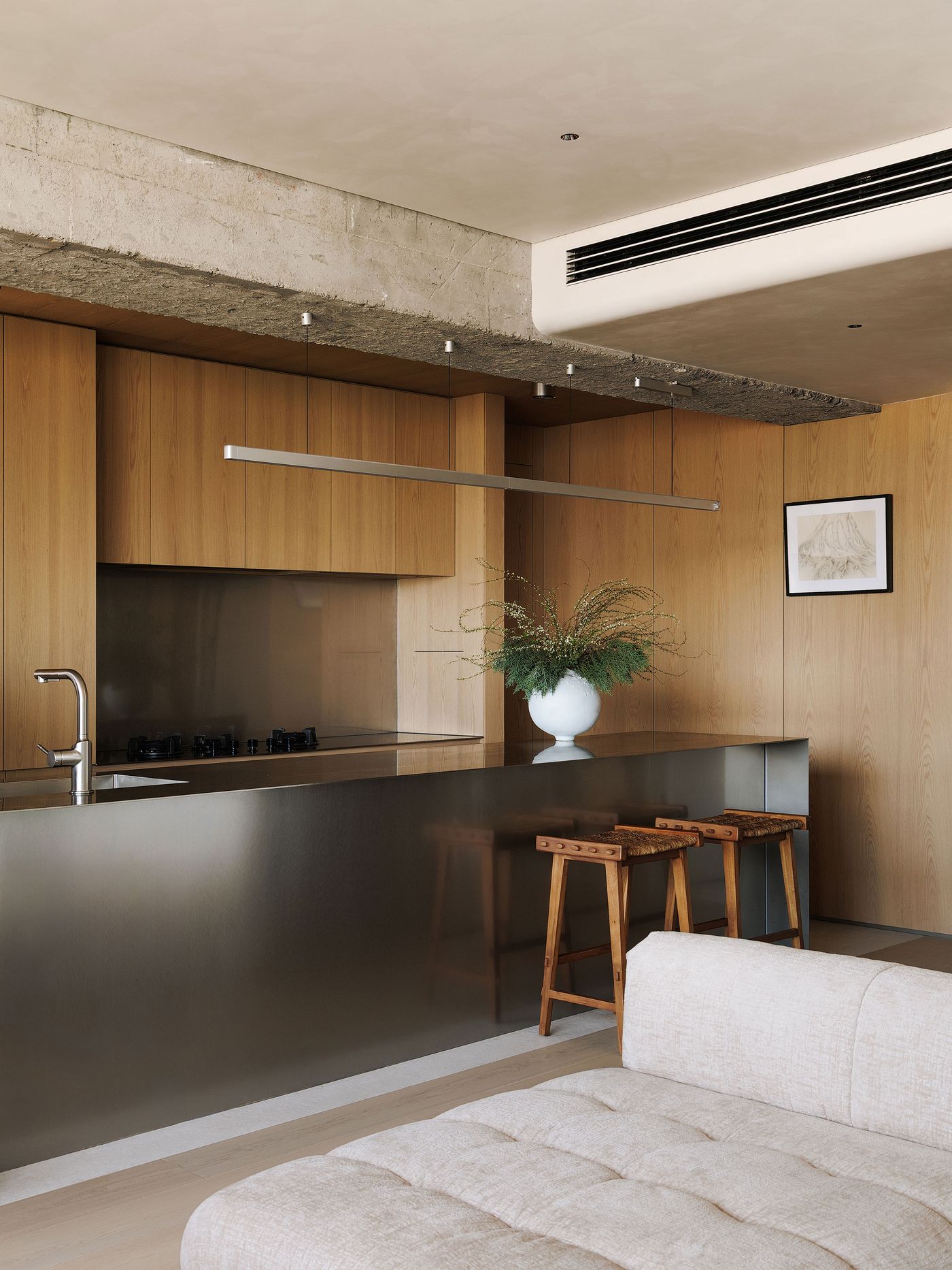 A modern open-plan kitchen and living area, showcasing a sophisticated material palette. The kitchen features custom oak cabinetry, a large brushed stainless steel island with integrated sink, and minimalist pendant lighting. An inviting cream-colored modular sofa anchors the foreground, reflecting the YSP Design's balance of warmth and contemporary functionality. A modern open-plan kitchen and living area, showcasing a sophisticated material palette. The kitchen features custom oak cabinetry, a large brushed stainless steel island with integrated sink, and minimalist pendant lighting. An inviting cream-colored modular sofa anchors the foreground, reflecting the YSP Design's balance of warmth and contemporary functionality.