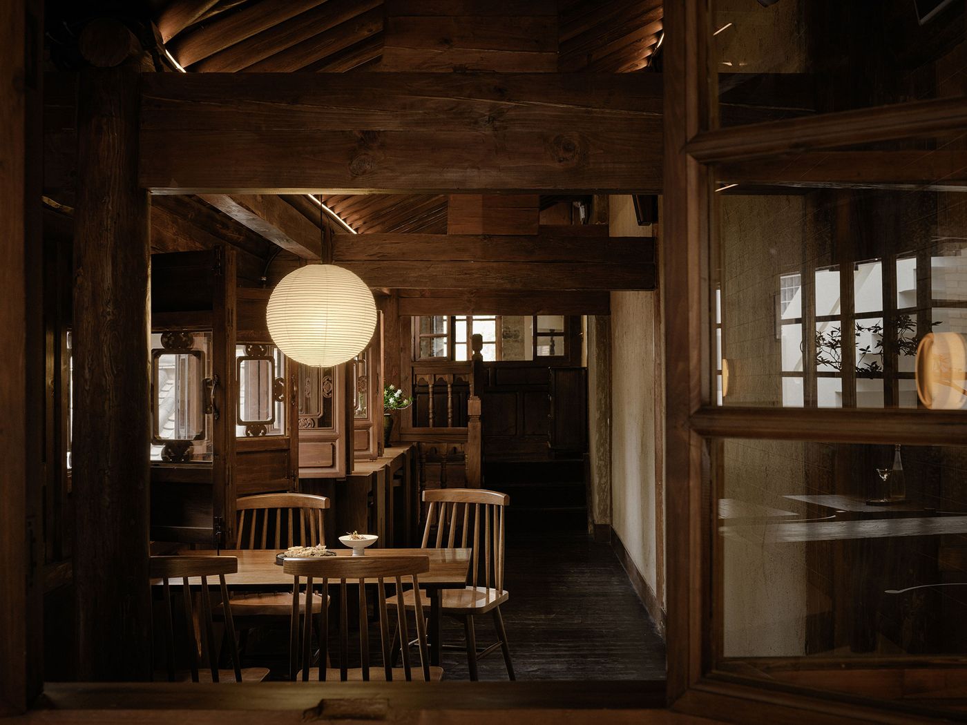 Cozy wooden interior of a restaurant featuring warm lighting, round paper lantern, and wooden furniture, creating a welcoming atmosphere. Cozy wooden interior of a restaurant featuring warm lighting, round paper lantern, and wooden furniture, creating a welcoming atmosphere.