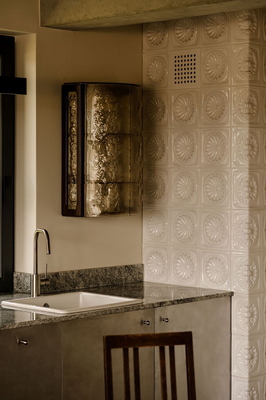 A modern kitchen corner features a stainless steel sink, a textured gold cabinet, and intricate white tile backsplash. A modern kitchen corner features a stainless steel sink, a textured gold cabinet, and intricate white tile backsplash.