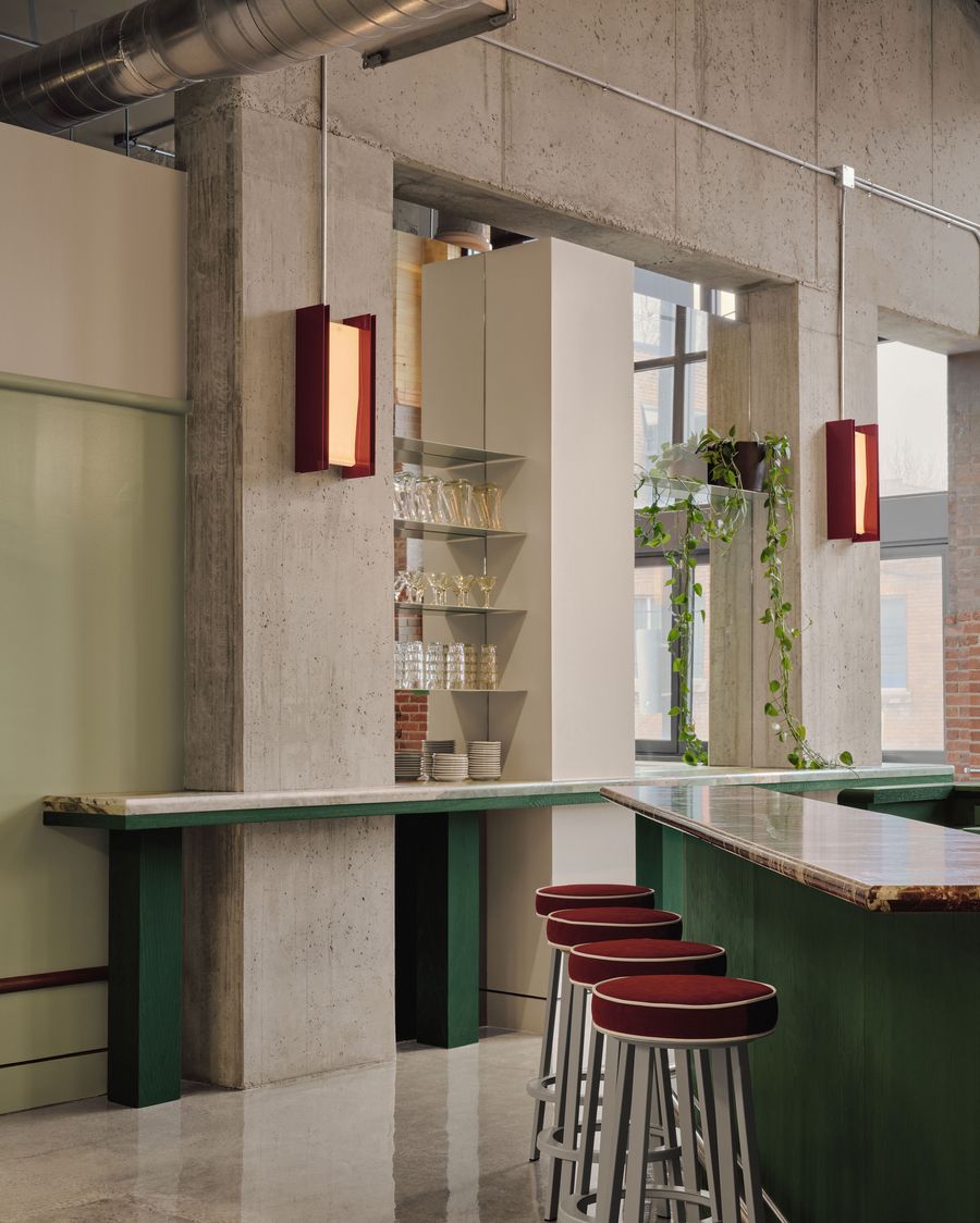 Modern bar with concrete walls, green accents, elegant bar stools, and shelves displaying glassware, enhanced by natural light. Modern bar with concrete walls, green accents, elegant bar stools, and shelves displaying glassware, enhanced by natural light.