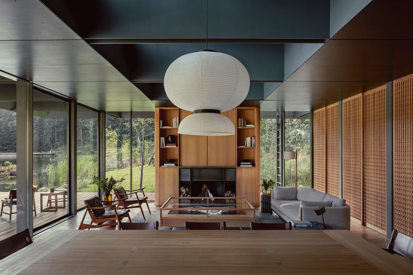 Modern living space featuring large windows, a central fireplace, a minimalist sofa, and a paper lantern pendant light illuminating the room.