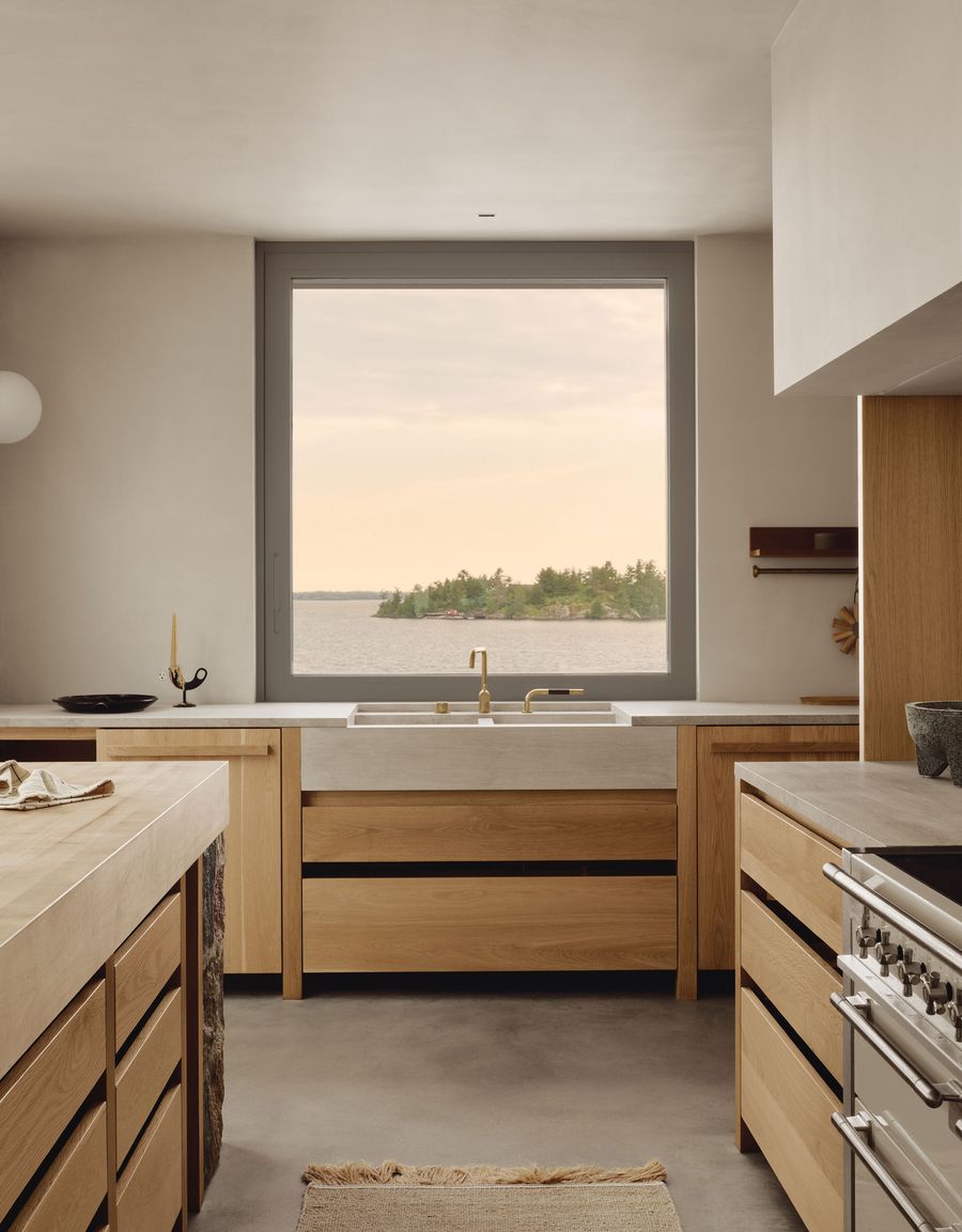 Modern kitchen with wooden cabinetry, a double sink, and large window showcasing a scenic lakeside view. Soft natural lighting fills the space.