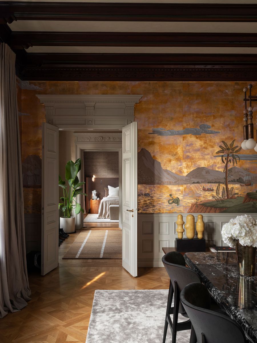 A spacious, elegantly designed interior featuring a mural, dark wood beams, and a view into a cozy bedroom.