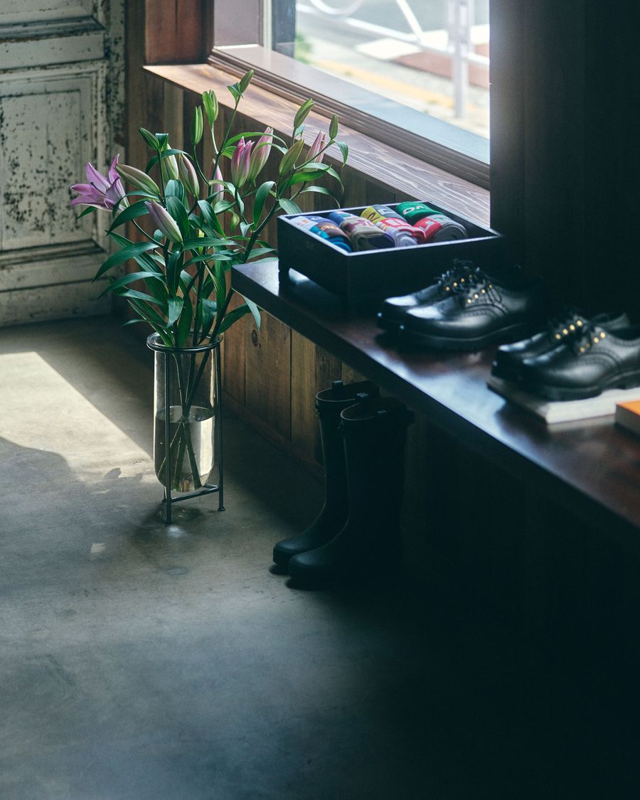 A modern interior scene featuring a vase of lilies, a box of colorful socks, black shoes, and rubber boots on a wooden shelf.
