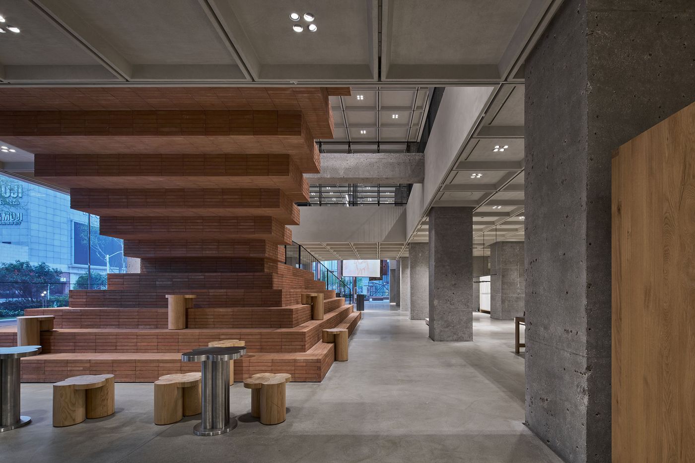 An interior space featuring a striking red brick staircase, wooden stools, and concrete pillars, blending modern design elements. An interior space featuring a striking red brick staircase, wooden stools, and concrete pillars, blending modern design elements.