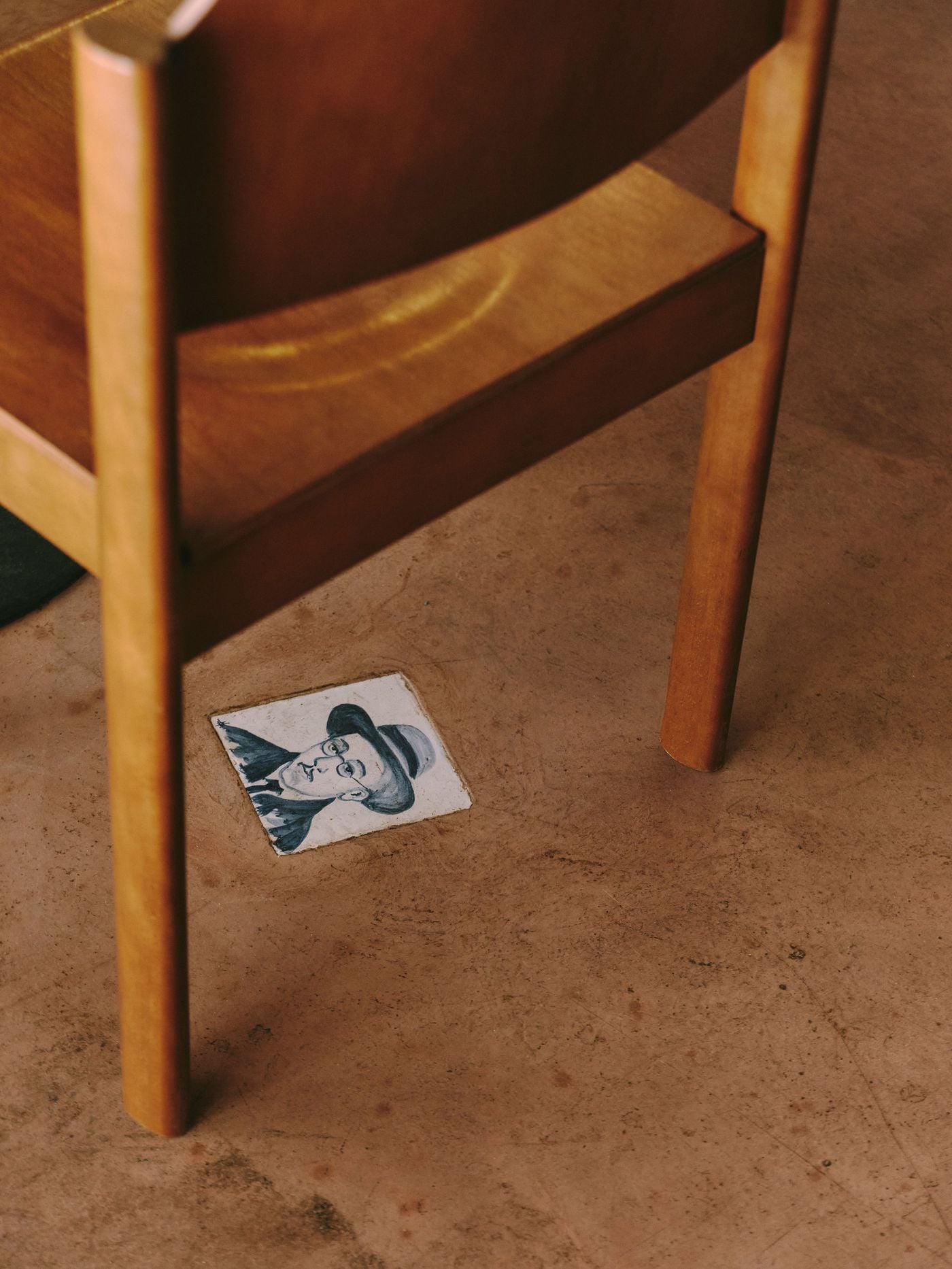 A single hand-painted azulejo is set into the cement floor at SaltoBar in Paris, almost like a found artefact. Its cobalt brushwork depicts a bespectacled man in a brimmed hat. The tile peeks out beside the leg of a vintage wooden chair, a playful discovery underfoot.
