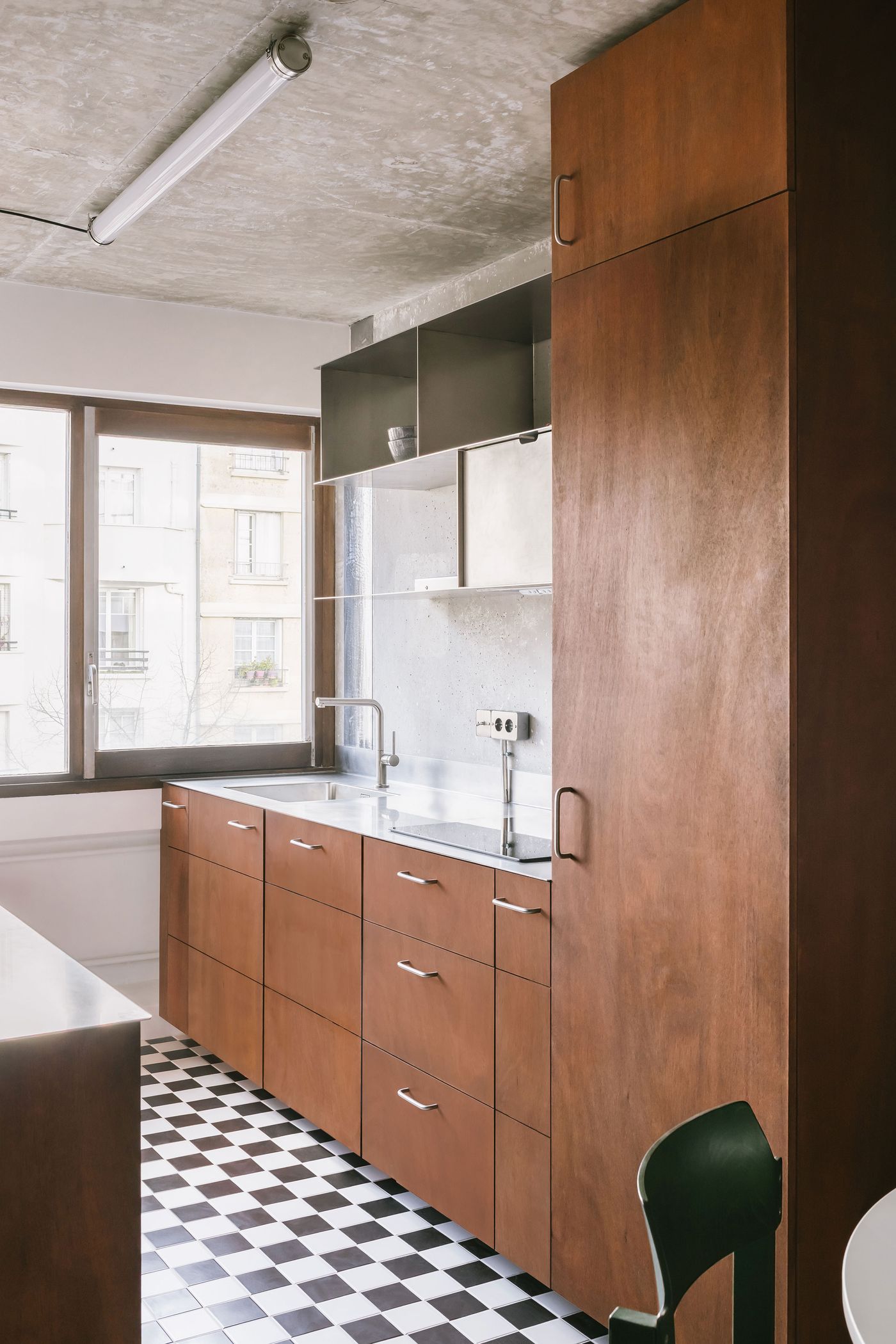 Modern kitchen featuring sleek wooden cabinets, stainless steel countertops, and a black-and-white checkered floor, with ample natural light. Modern kitchen featuring sleek wooden cabinets, stainless steel countertops, and a black-and-white checkered floor, with ample natural light.