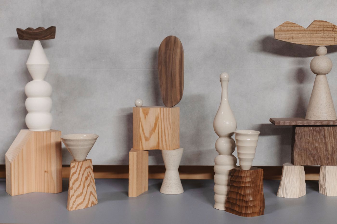 A collection of modern wooden and ceramic sculptures in various shapes and sizes, artfully arranged on a gray background.