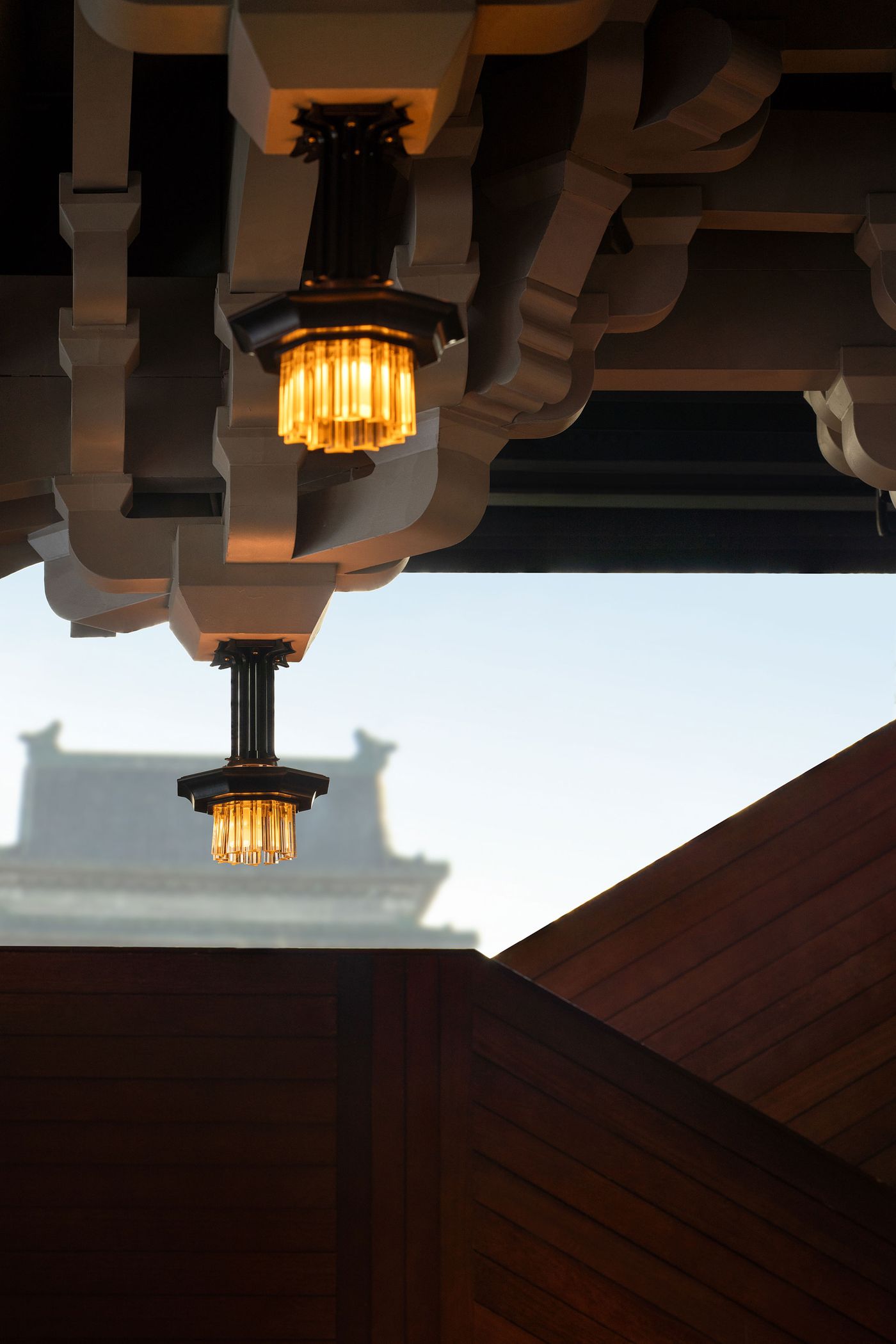 Elaborate ceiling with geometric patterns and vintage-style pendant lights, framed by warm wooden features and a blurred building in the background.