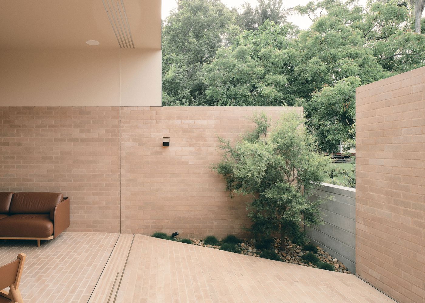 Contemporary outdoor space featuring a brown couch, textured brick walls, lush greenery, and a gently sloped stone pathway. Contemporary outdoor space featuring a brown couch, textured brick walls, lush greenery, and a gently sloped stone pathway.