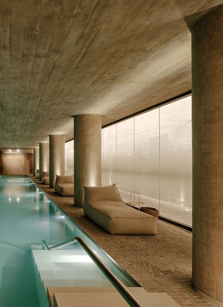 A serene indoor swimming pool at Ibaté, featuring a raw concrete ceiling and large, frosted glass panels that diffuse natural light, creating a tranquil atmosphere. Submerged lighting accentuates the water's surface, while minimalist lounge chairs invite relaxation, embodying a Zen-like contemporary design. A serene indoor swimming pool at Ibaté, featuring a raw concrete ceiling and large, frosted glass panels that diffuse natural light, creating a tranquil atmosphere. Submerged lighting accentuates the water's surface, while minimalist lounge chairs invite relaxation, embodying a Zen-like contemporary design.
