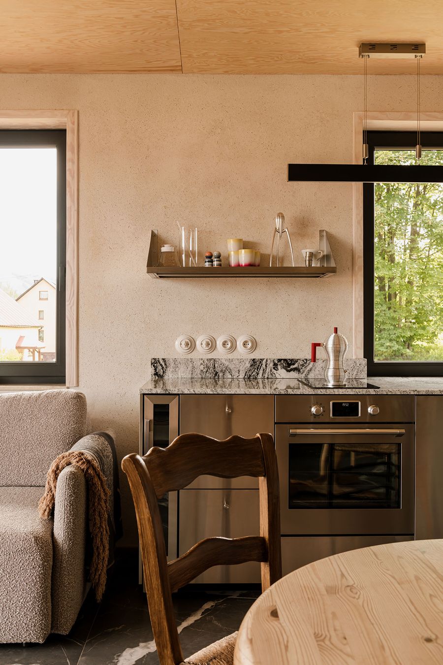 Modern kitchen featuring a marble countertop, stainless steel appliances, and a cozy seating area with a textured couch and wooden chair. Modern kitchen featuring a marble countertop, stainless steel appliances, and a cozy seating area with a textured couch and wooden chair.