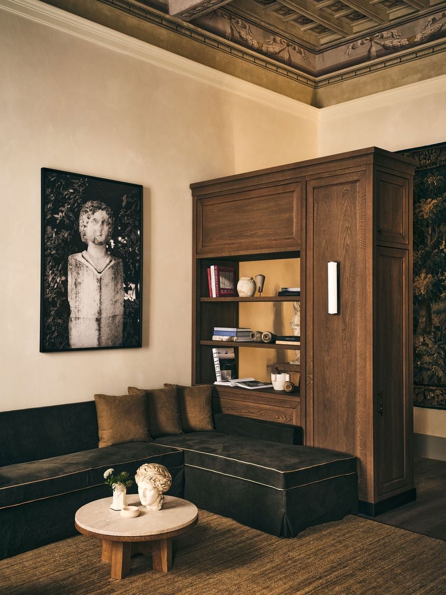 A large black-and-white photograph of a weathered classical bust hangs above a brown linen banquette in the lounge at La Réserve Firenze. An oak bookcase lit by a slim wall light, a round stone-topped table bearing a plaster head and a glimpse of the painted frieze above build a dialogue between antiquity and the present. A large black-and-white photograph of a weathered classical bust hangs above a brown linen banquette in the lounge at La Réserve Firenze. An oak bookcase lit by a slim wall light, a round stone-topped table bearing a plaster head and a glimpse of the painted frieze above build a dialogue between antiquity and the present.