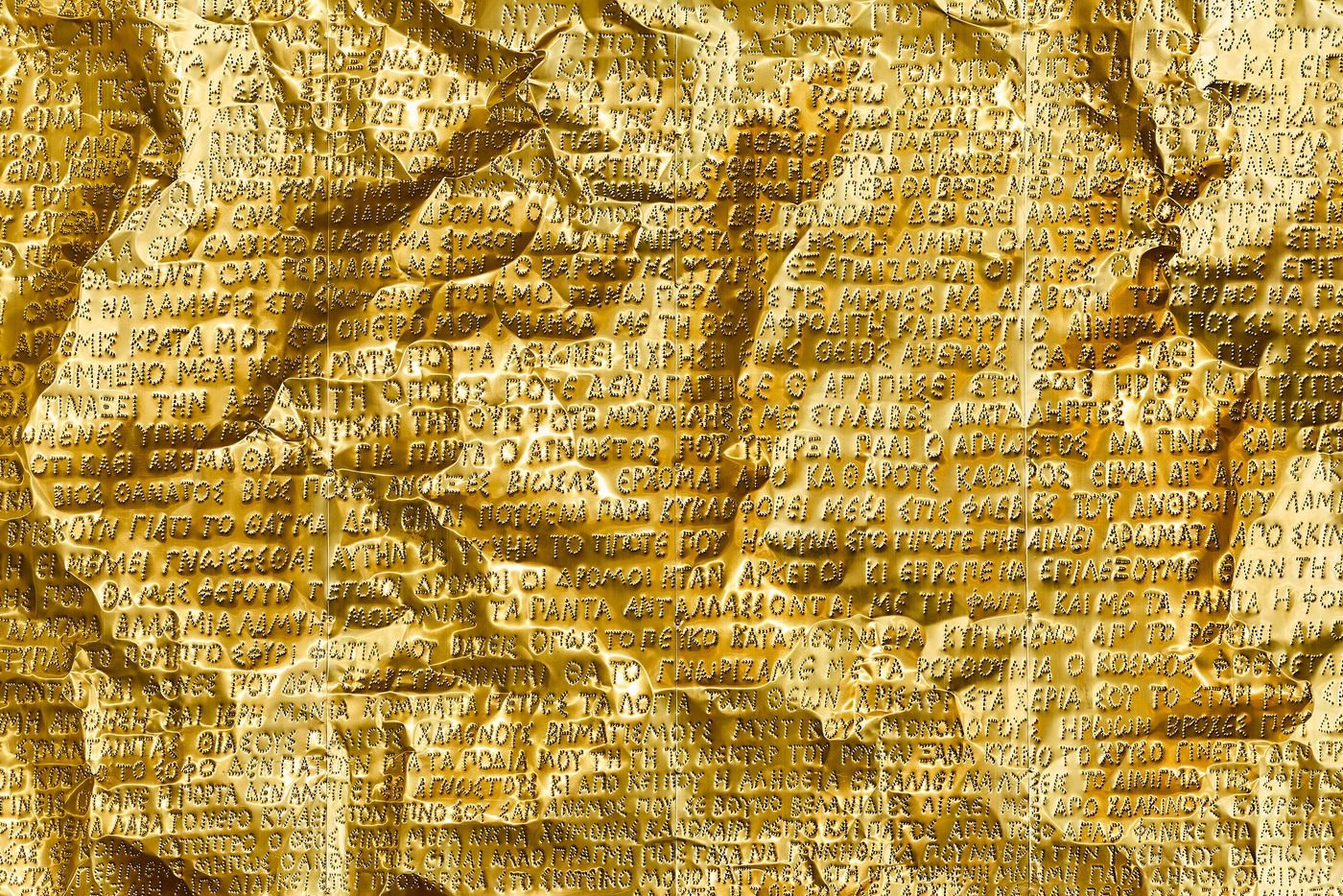 A highly detailed close-up of a golden metal sheet, part of Gabriel Leger's installation. The surface is densely etched with Greek script and text, creating a visually rich texture that appears both aged and contemporary. The lighting highlights the creases and folds of the crinkled metal, suggesting a reinterpretation of ancient parchment. A highly detailed close-up of a golden metal sheet, part of Gabriel Leger's installation. The surface is densely etched with Greek script and text, creating a visually rich texture that appears both aged and contemporary. The lighting highlights the creases and folds of the crinkled metal, suggesting a reinterpretation of ancient parchment.