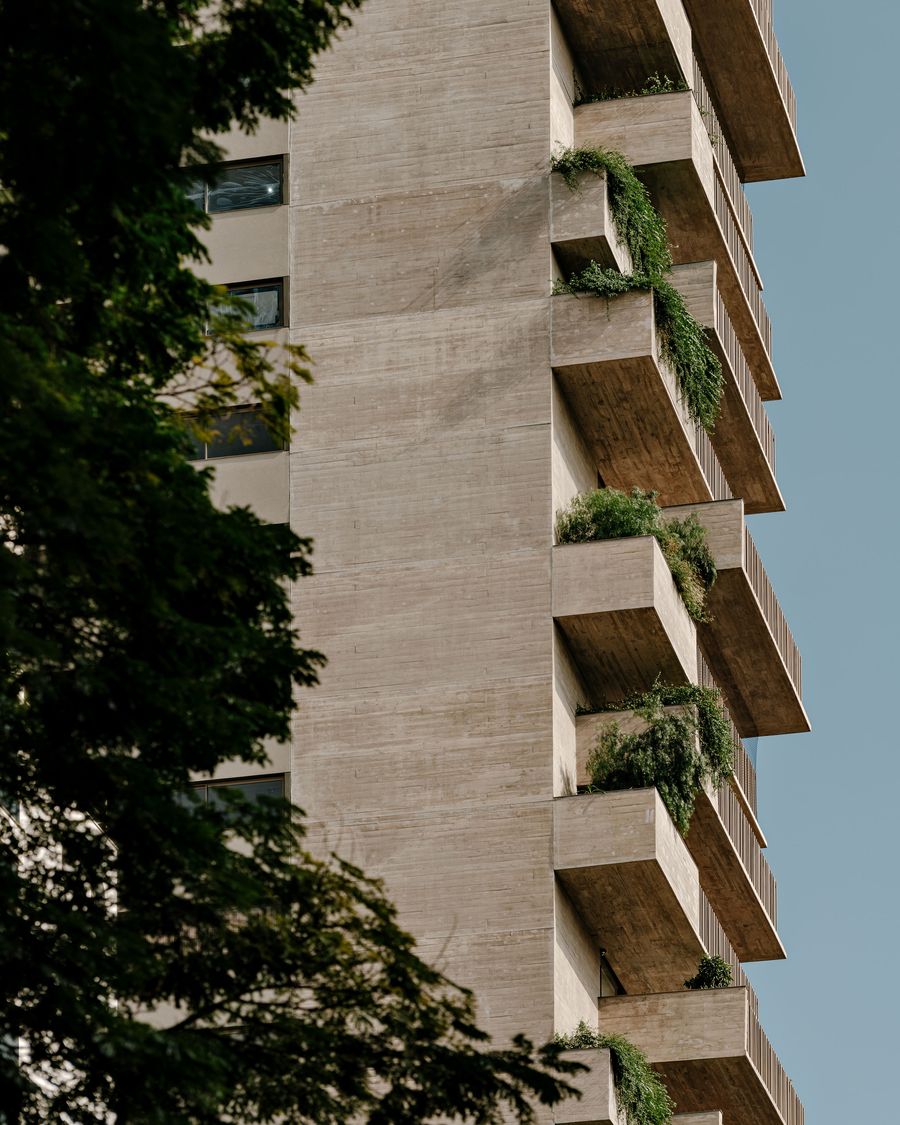 A vertical composition focusing on the textured concrete facade, where staggered balconies host cascading greenery. The interplay of rigid architectural lines and organic plant life highlights the building's biophilic design, softening its brutalist origins. A vertical composition focusing on the textured concrete facade, where staggered balconies host cascading greenery. The interplay of rigid architectural lines and organic plant life highlights the building's biophilic design, softening its brutalist origins.