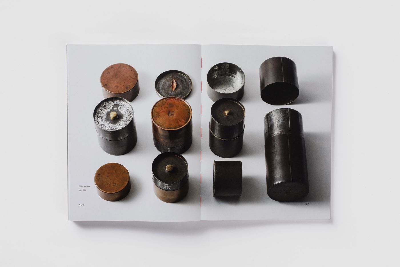 An open book displaying a collection of vintage metal containers in various sizes and finishes on a plain white background. An open book displaying a collection of vintage metal containers in various sizes and finishes on a plain white background.