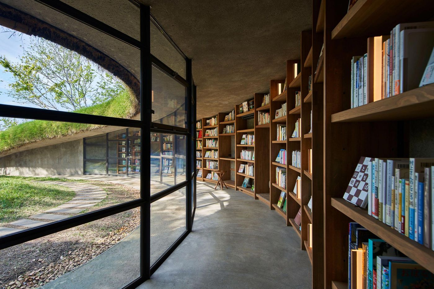 A cozy library interior features curved wood shelves filled with books, large windows, and a view of greenery outside. A cozy library interior features curved wood shelves filled with books, large windows, and a view of greenery outside.