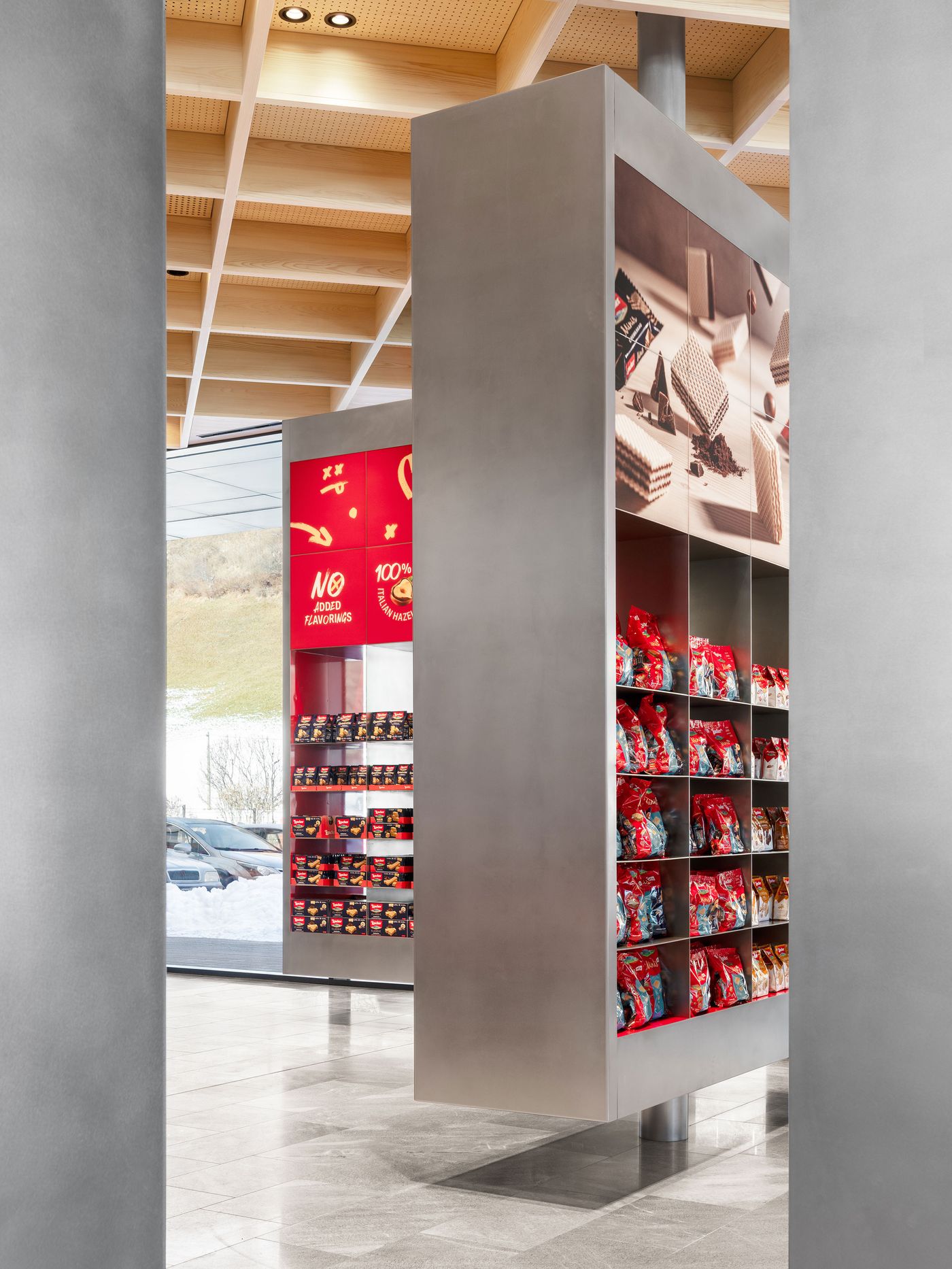 A towering product wall creates retail theater through systematic organization and dramatic scale. Strategic lighting illuminates the merchandise grid while maintaining architectural sophistication through clean lines and neutral materials, demonstrating how commercial display can achieve museum-quality aesthetic impact.