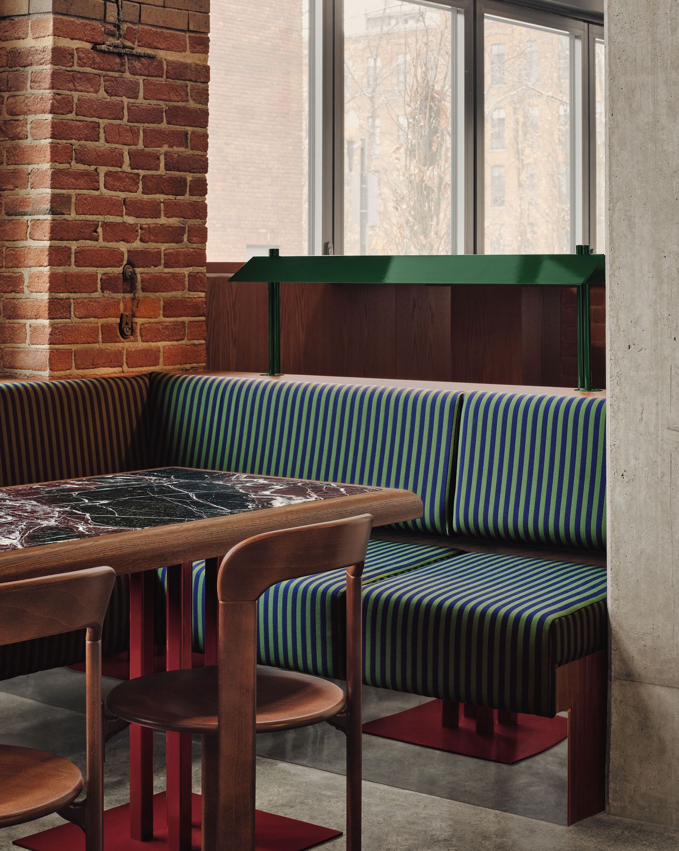 Modern dining area featuring a marble tabletop, striped upholstery, and a mix of wood and metal elements against a brick wall.