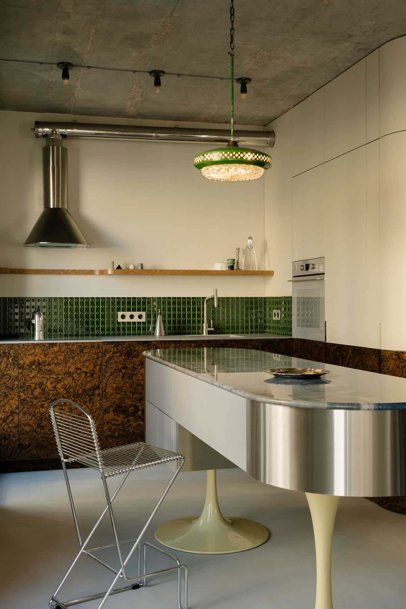 Under a vintage green pendant, the kitchen’s materials come alive: fluted steel, marbled wood cabinetry, and bottle-green tiles create a palette that balances boldness with a sense of crafted restraint.