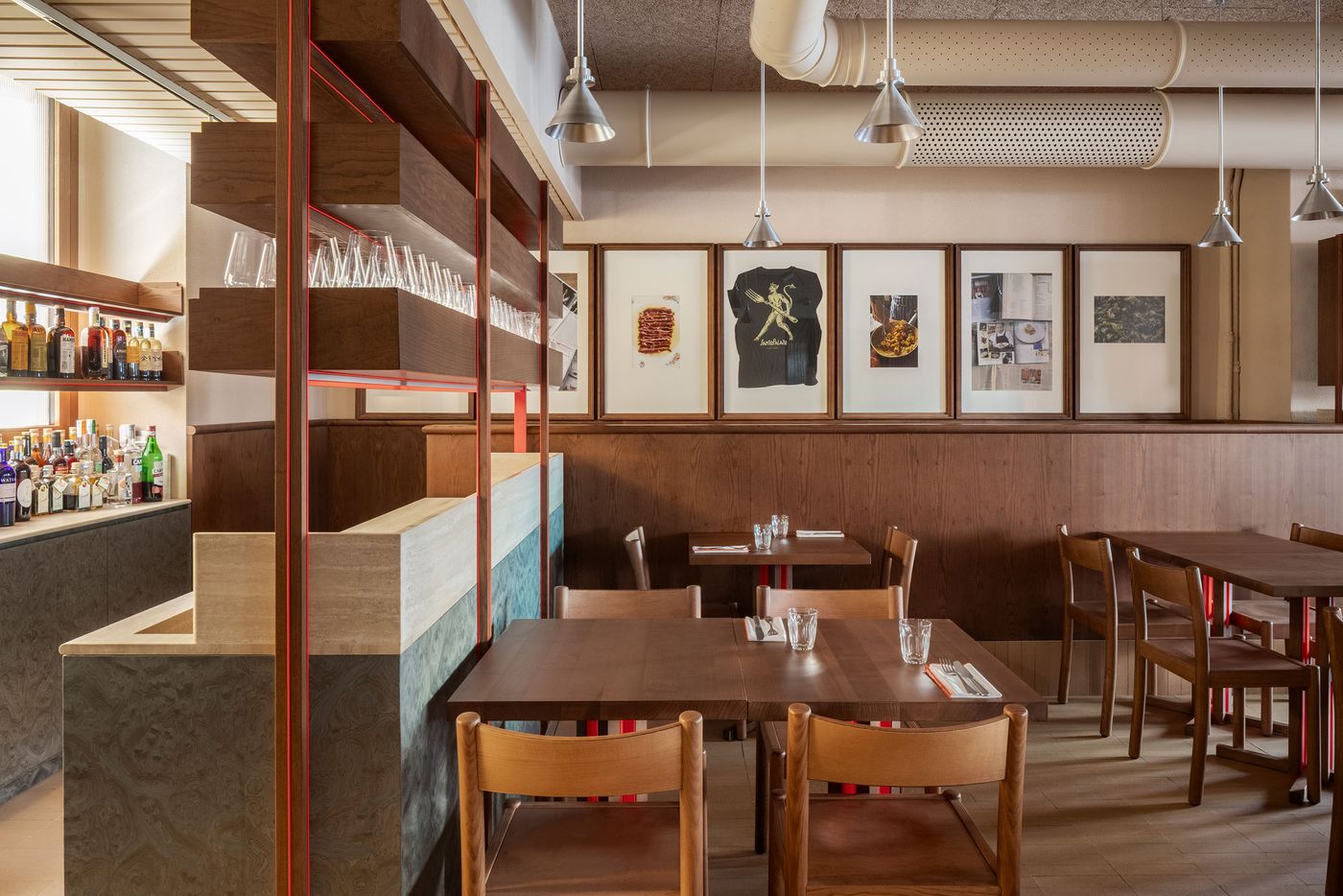 Santo Palato's dining area by Naessi Studio, showcasing an eclectic mix of materials and textures. A custom-designed shelving unit with orange accents and textured grey panels creates a stylish room divider near a bar area. Framed artworks adorn the wood-paneled walls, lending an authentic, art-infused atmosphere to the modern trattoria. Santo Palato's dining area by Naessi Studio, showcasing an eclectic mix of materials and textures. A custom-designed shelving unit with orange accents and textured grey panels creates a stylish room divider near a bar area. Framed artworks adorn the wood-paneled walls, lending an authentic, art-infused atmosphere to the modern trattoria.