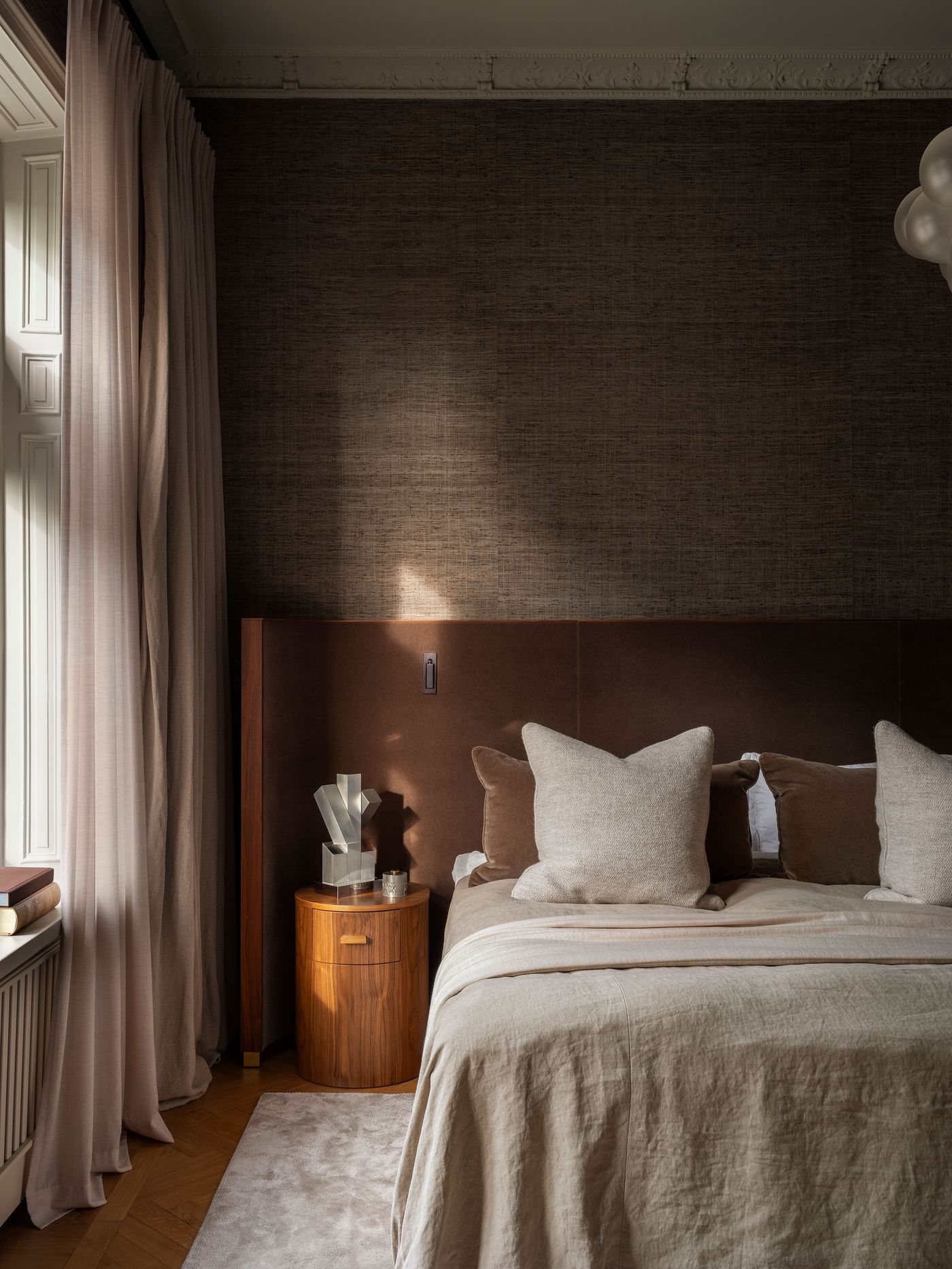 Cozy bedroom corner with a brown upholstered headboard, plush pillows, wooden nightstand, and soft lighting from a window. Cozy bedroom corner with a brown upholstered headboard, plush pillows, wooden nightstand, and soft lighting from a window.