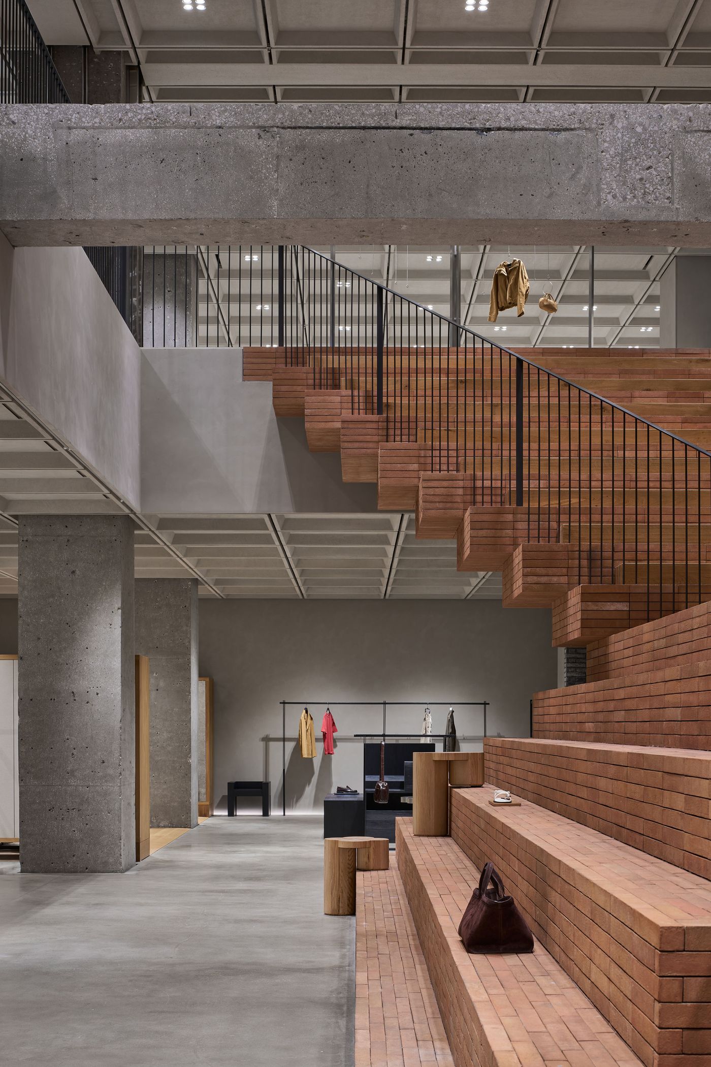 Interior of a modern retail space featuring wooden stairs, hanging garments, concrete walls, and minimalist decor. Interior of a modern retail space featuring wooden stairs, hanging garments, concrete walls, and minimalist decor.