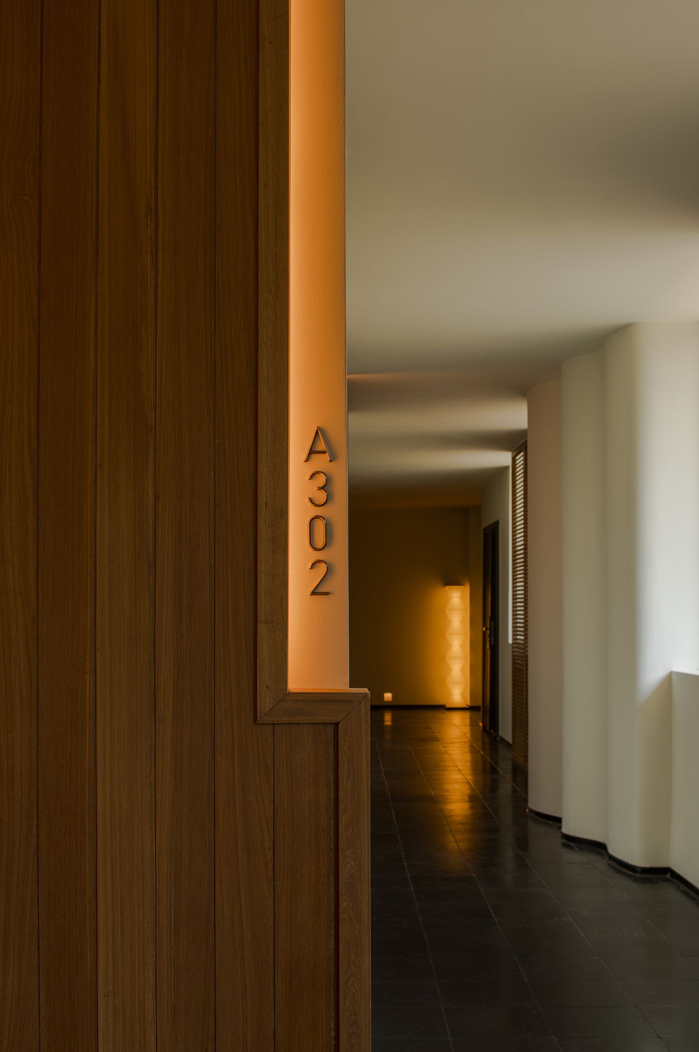 Stylish wooden wall with illuminated room number A302, leading to a softly lit hallway with modern design elements. Stylish wooden wall with illuminated room number A302, leading to a softly lit hallway with modern design elements.