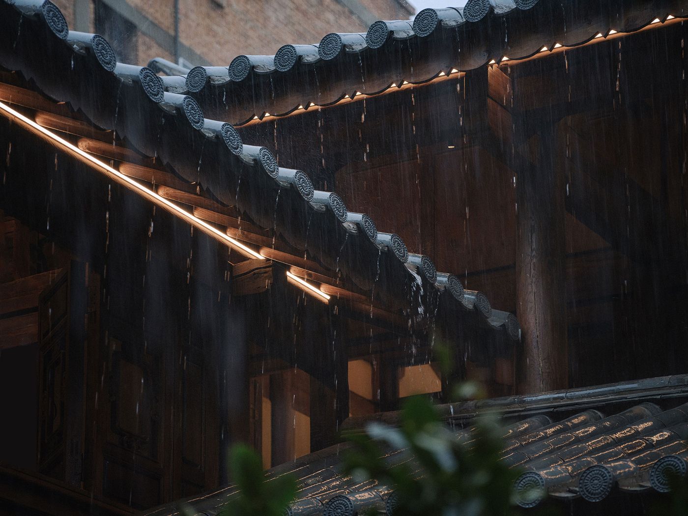 Rainwater cascades from traditional tiled eaves, illuminated by soft lighting, capturing a serene, moody atmosphere. Rainwater cascades from traditional tiled eaves, illuminated by soft lighting, capturing a serene, moody atmosphere.