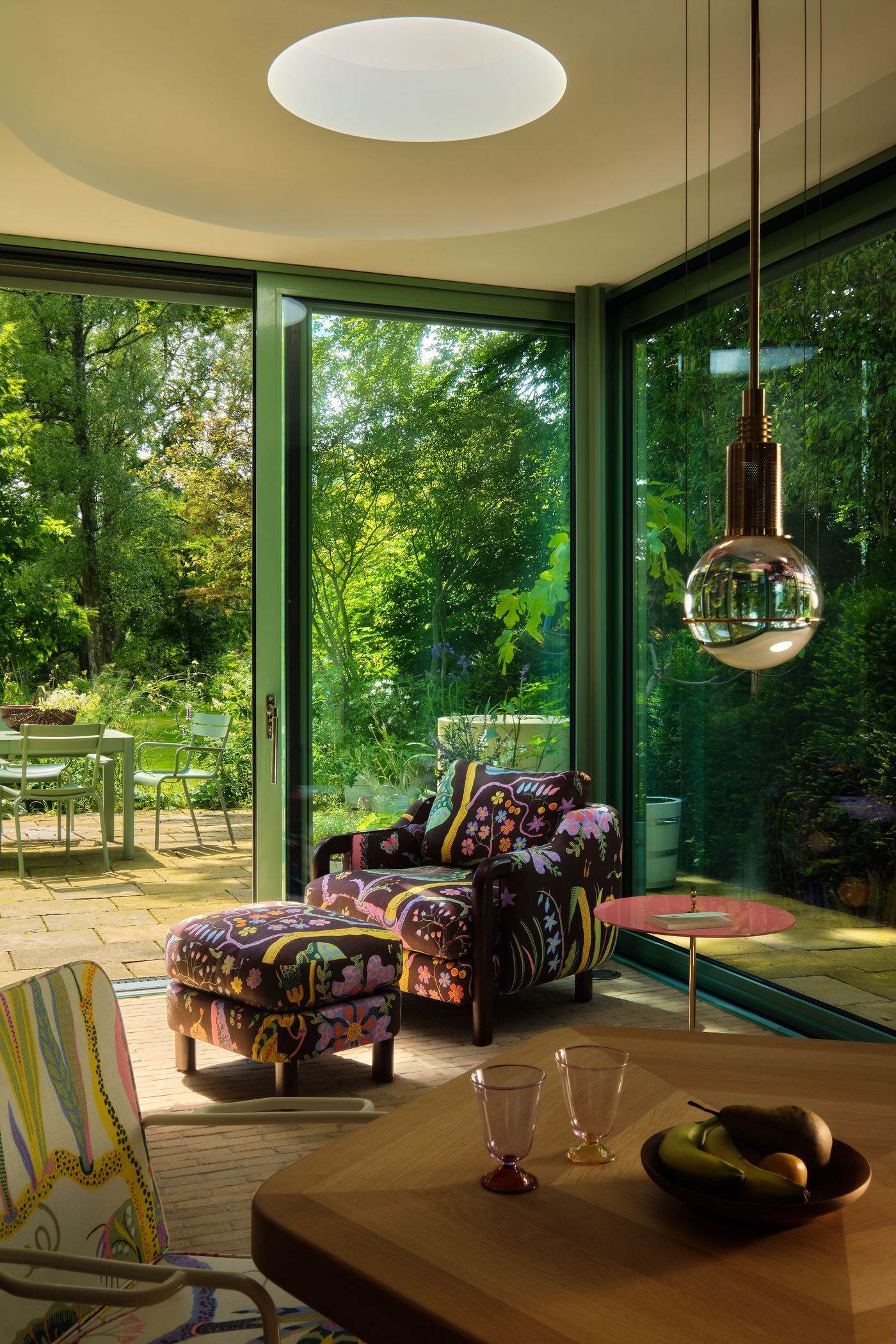 A cozy, colorful seating area with a floral chair, vibrant decor, and large glass doors opening to a lush garden outside.