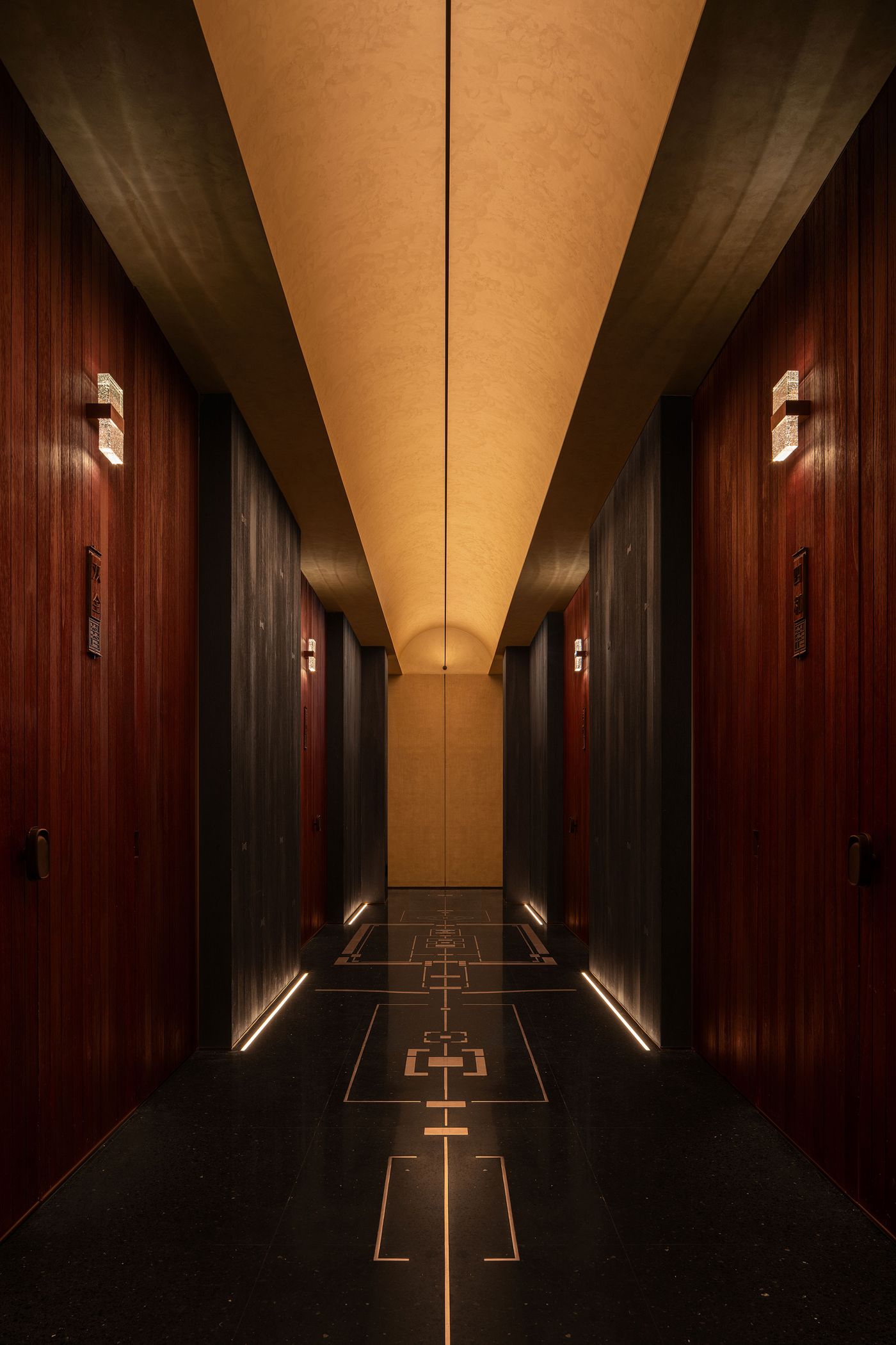 A stylish corridor with wood-paneled doors, ambient lighting, and elegant patterned flooring leading to a subtly lit end. A stylish corridor with wood-paneled doors, ambient lighting, and elegant patterned flooring leading to a subtly lit end.