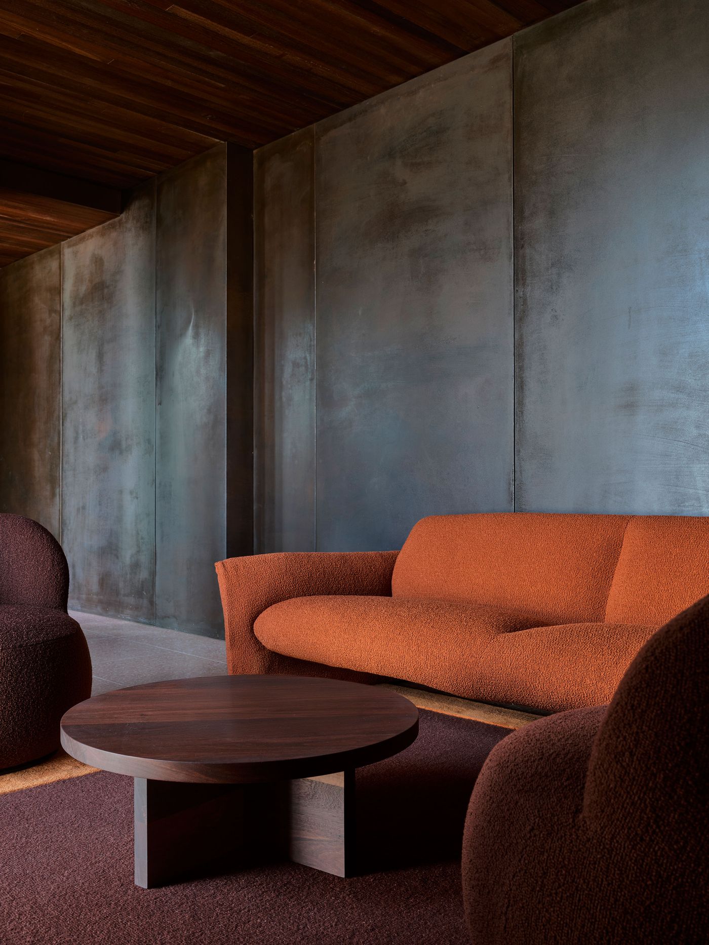 A cozy seating area features an orange textured couch and two round, brown upholstered chairs, accented by a circular wooden coffee table. A cozy seating area features an orange textured couch and two round, brown upholstered chairs, accented by a circular wooden coffee table.