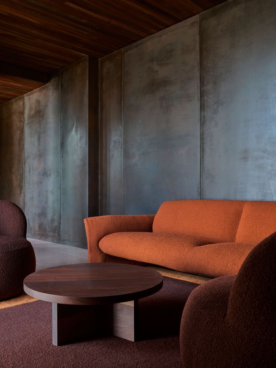 A cozy seating area features an orange textured couch and two round, brown upholstered chairs, accented by a circular wooden coffee table. A cozy seating area features an orange textured couch and two round, brown upholstered chairs, accented by a circular wooden coffee table.