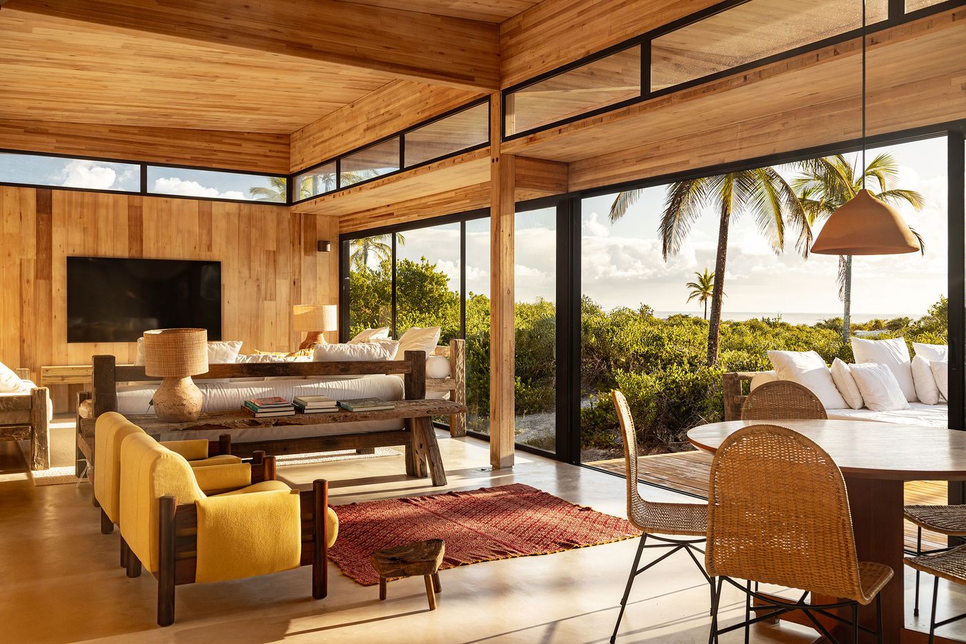 An inviting open-plan living space features a harmonious blend of light wood ceilings and walls, with distinct yellow armchairs and a raw timber coffee table. Expansive windows frame lush tropical views, connecting the interior's minimalist lines and natural materials to the vibrant outdoors. An inviting open-plan living space features a harmonious blend of light wood ceilings and walls, with distinct yellow armchairs and a raw timber coffee table. Expansive windows frame lush tropical views, connecting the interior's minimalist lines and natural materials to the vibrant outdoors.