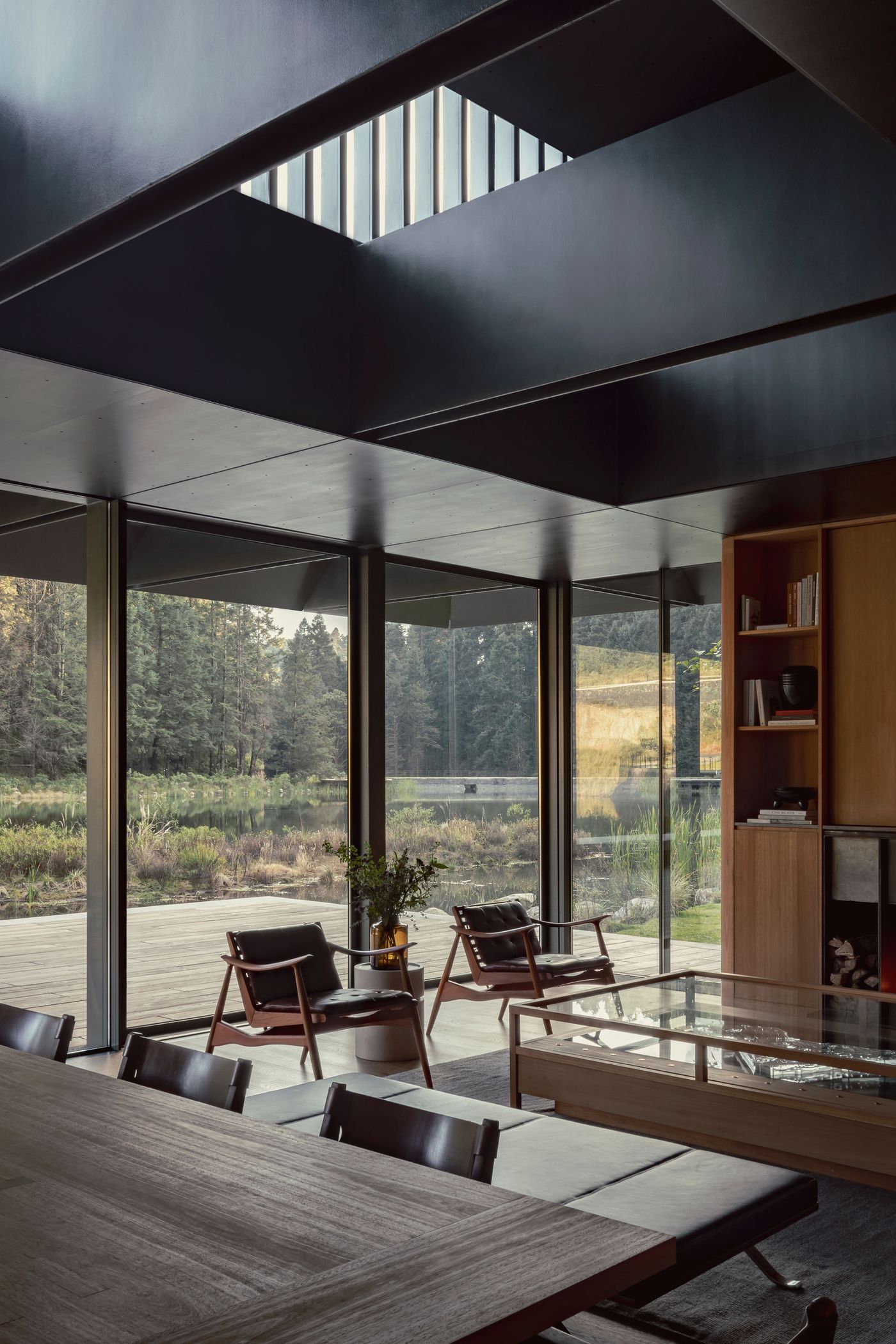 Modern interior with panoramic glass walls, wooden furniture, and a view of tranquil nature, creating a serene, open atmosphere.
