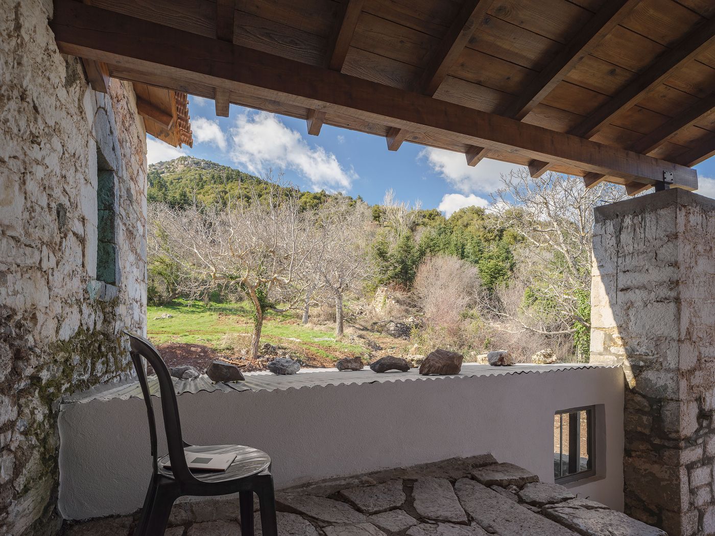 Exposed timber rafters frame the hillside vista from this contemplative terrace space, where weathered stone walls meet contemporary concrete interventions. The composition celebrates the building's integration with its natural setting, creating intimate outdoor rooms that capture both heritage and landscape.