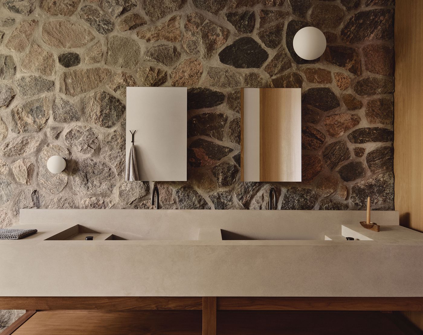 Modern bathroom featuring a stone wall, minimalist sinks, dual mirrors, and sleek fixtures, exuding a warm, organic aesthetic. Modern bathroom featuring a stone wall, minimalist sinks, dual mirrors, and sleek fixtures, exuding a warm, organic aesthetic.