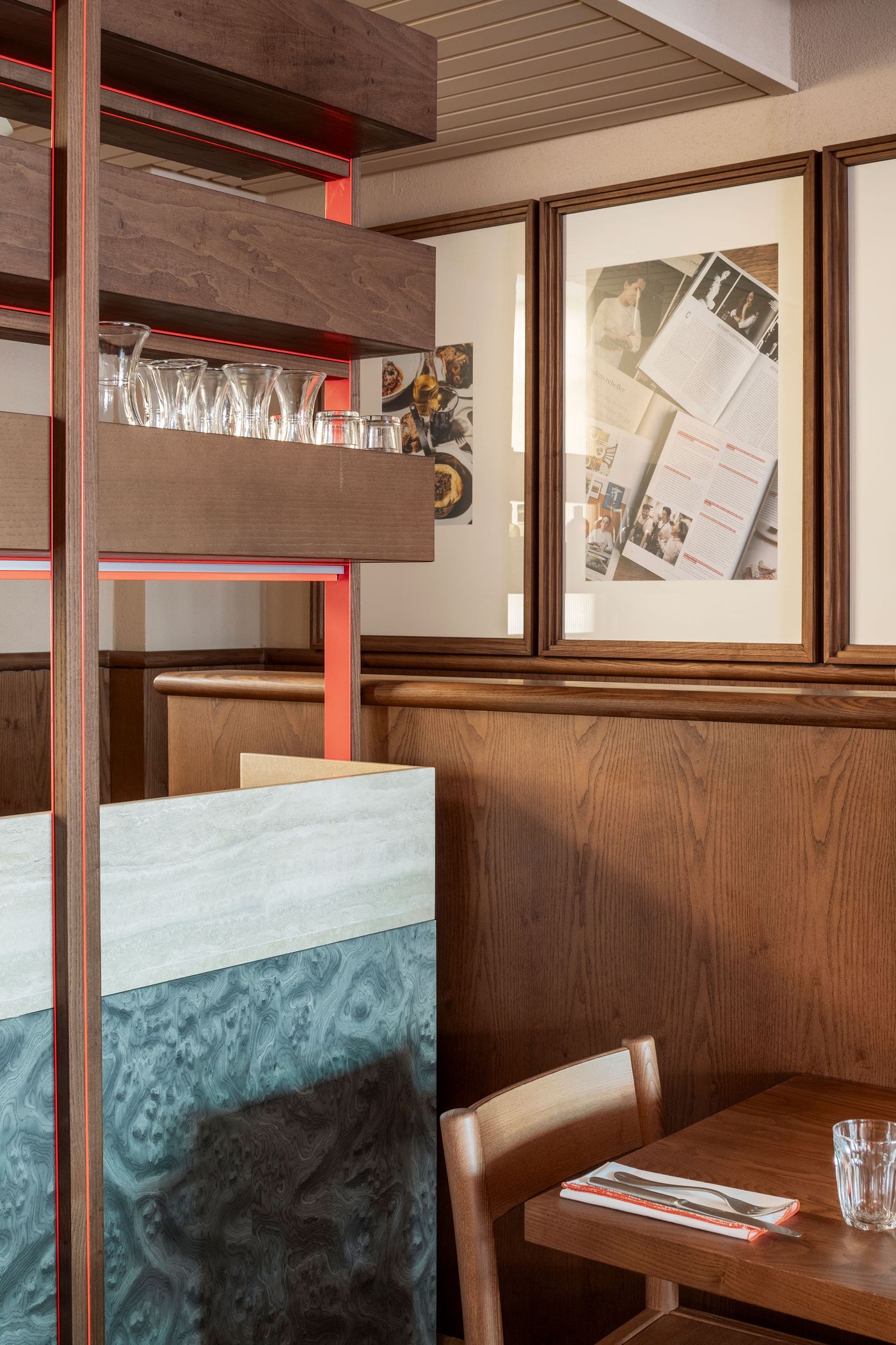 A detailed view of Santo Palato by Naessi Studio, highlighting an innovative modular shelving system crafted from warm wood with subtle orange-red interior accents. Glasses are neatly arranged on the shelves, while framed artworks on the wood-paneled wall and the textured, multi-toned partition in the foreground reveal a meticulous attention to material play. A detailed view of Santo Palato by Naessi Studio, highlighting an innovative modular shelving system crafted from warm wood with subtle orange-red interior accents. Glasses are neatly arranged on the shelves, while framed artworks on the wood-paneled wall and the textured, multi-toned partition in the foreground reveal a meticulous attention to material play.