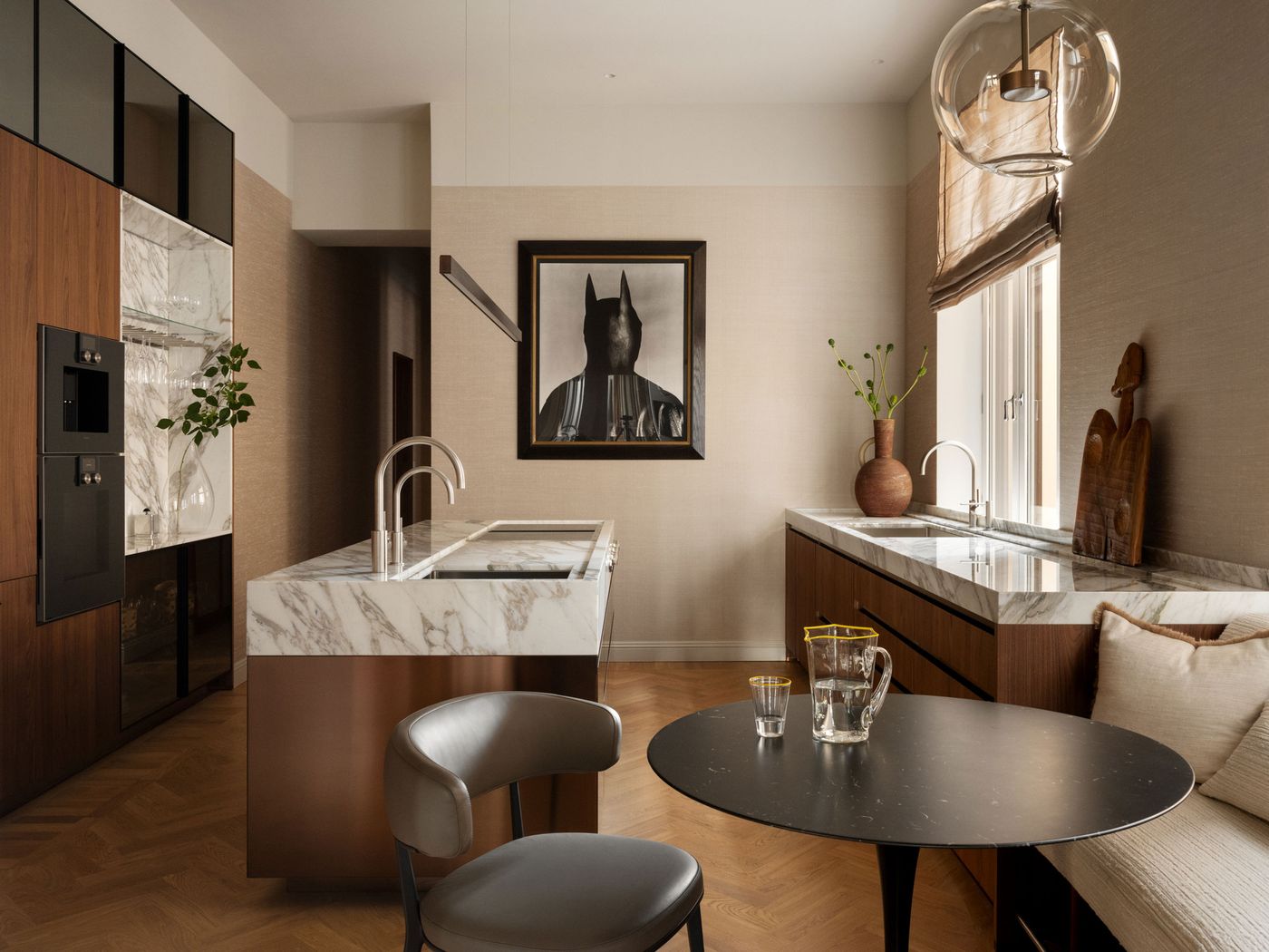 A modern kitchen featuring marble countertops, wood cabinetry, stylish decor, and a striking Batman portrait on the wall. A modern kitchen featuring marble countertops, wood cabinetry, stylish decor, and a striking Batman portrait on the wall.