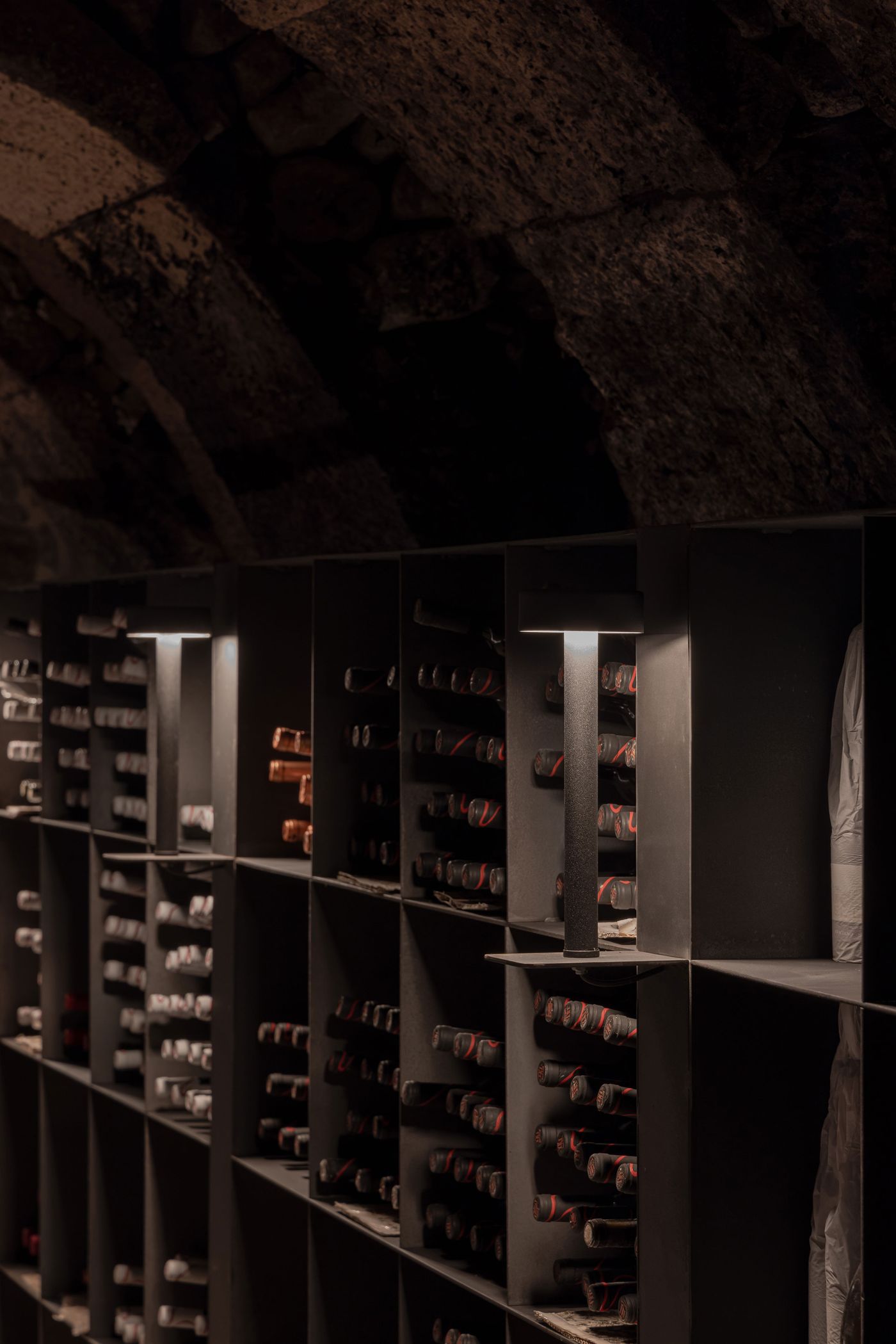 A dimly lit wine cellar showcasing neatly arranged wine bottles on dark shelves, with modern lighting illuminating the space. A dimly lit wine cellar showcasing neatly arranged wine bottles on dark shelves, with modern lighting illuminating the space.
