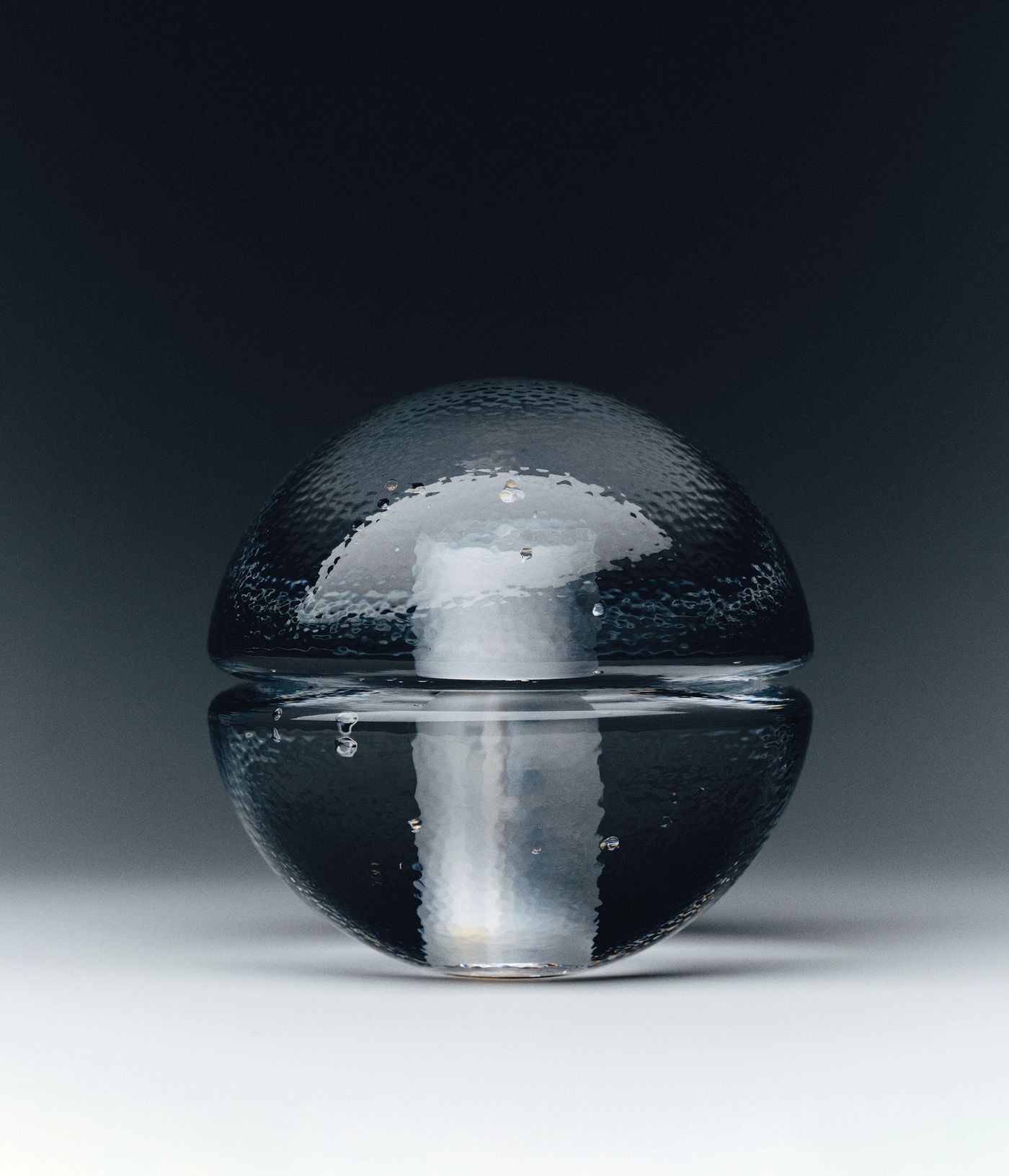 A clear, textured bocci 14p lamp is centered against a dark background. The orb’s surface features small bubbles, and the candle within creates a soft, diffused glow.