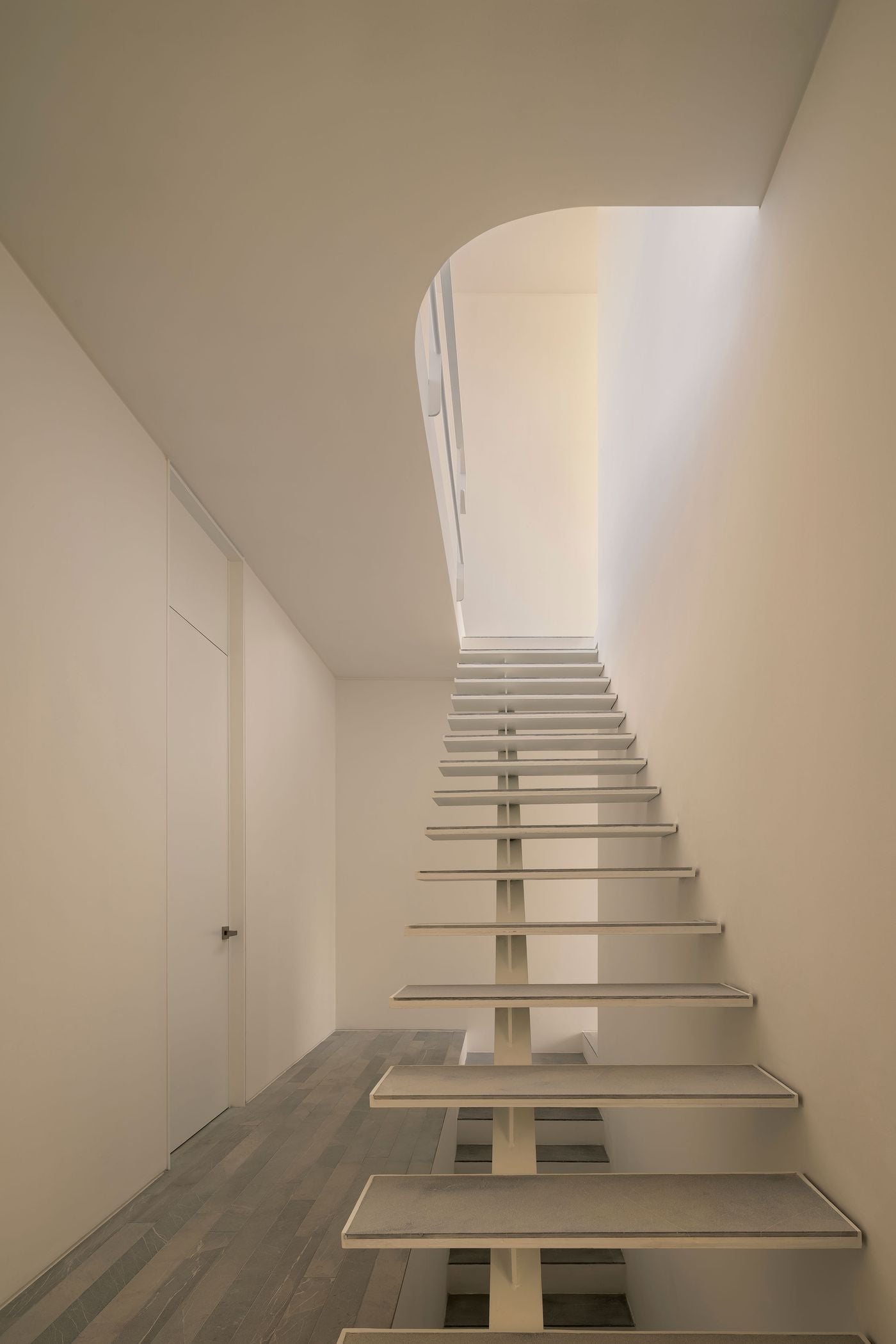A lightweight open-riser staircase climbs through Casa Tlaloc around a slender central spine, its pale grey treads appearing to float against white walls. Daylight pours down from the upper level through a softly curved ceiling opening, turning the compact circulation space into one of the house’s most sculptural architectural moments. A lightweight open-riser staircase climbs through Casa Tlaloc around a slender central spine, its pale grey treads appearing to float against white walls. Daylight pours down from the upper level through a softly curved ceiling opening, turning the compact circulation space into one of the house’s most sculptural architectural moments.