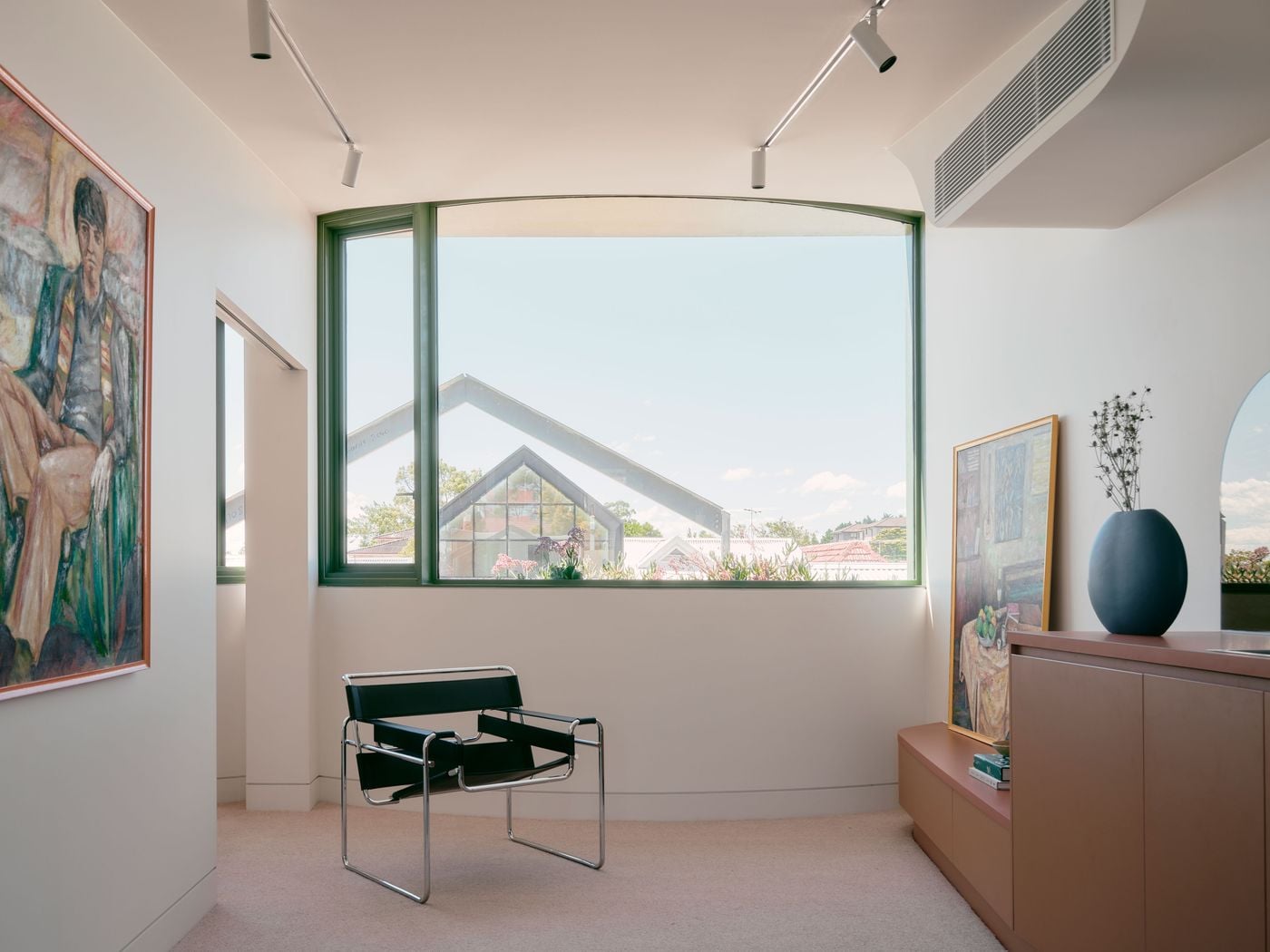 The studio’s living area gathers around a broad curved window overlooking the laneway and surrounding rooftops. Sage-green framing traces the concave façade, while a black tubular-steel chair, terracotta cabinetry and loosely displayed paintings lend the otherwise pared-back interior a subtly eclectic, art-filled character. The studio’s living area gathers around a broad curved window overlooking the laneway and surrounding rooftops. Sage-green framing traces the concave façade, while a black tubular-steel chair, terracotta cabinetry and loosely displayed paintings lend the otherwise pared-back interior a subtly eclectic, art-filled character.